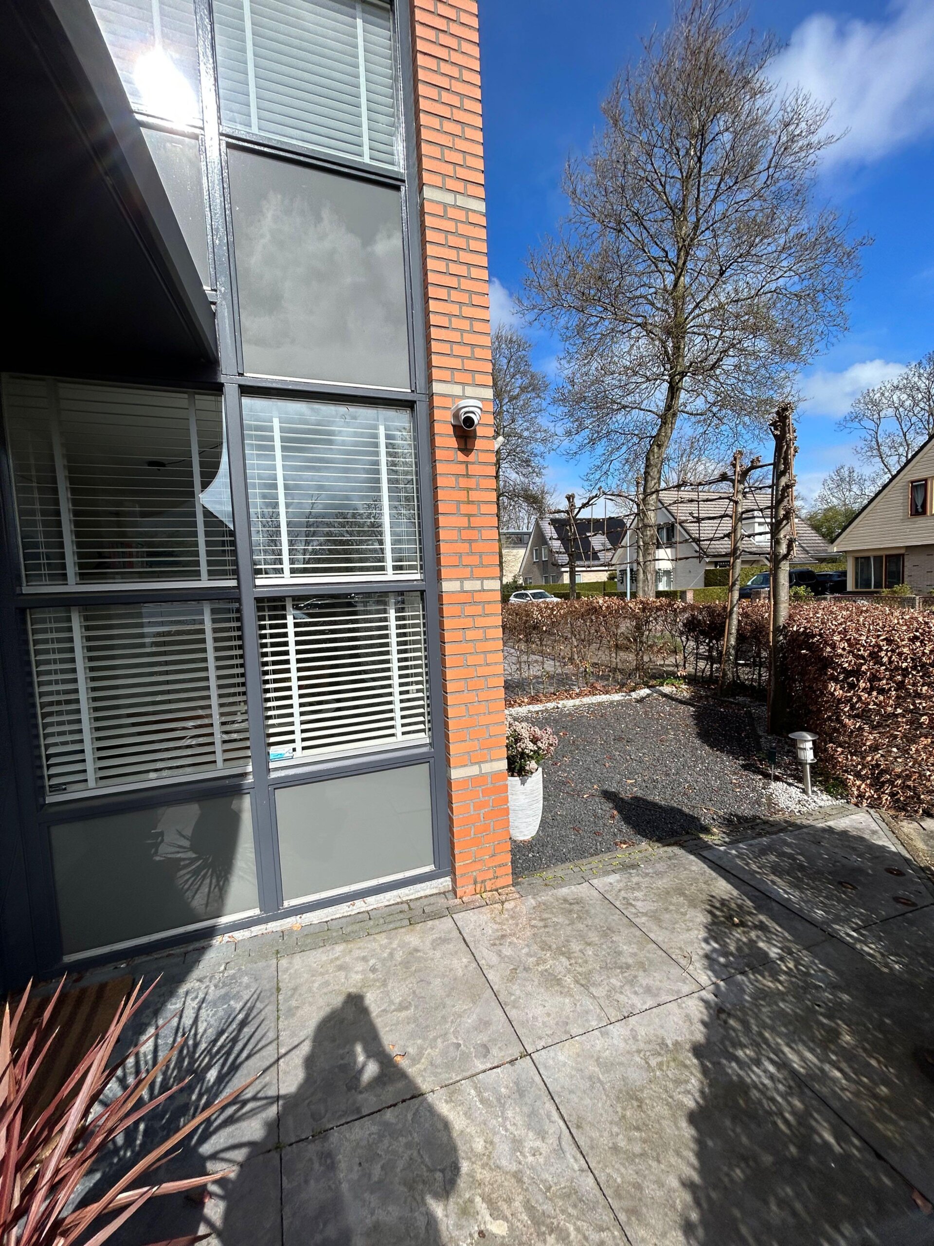 Witte Dahua bewakingscamera op de hoek van een moderne woning met rode baksteen, gericht op de tuin en oprit