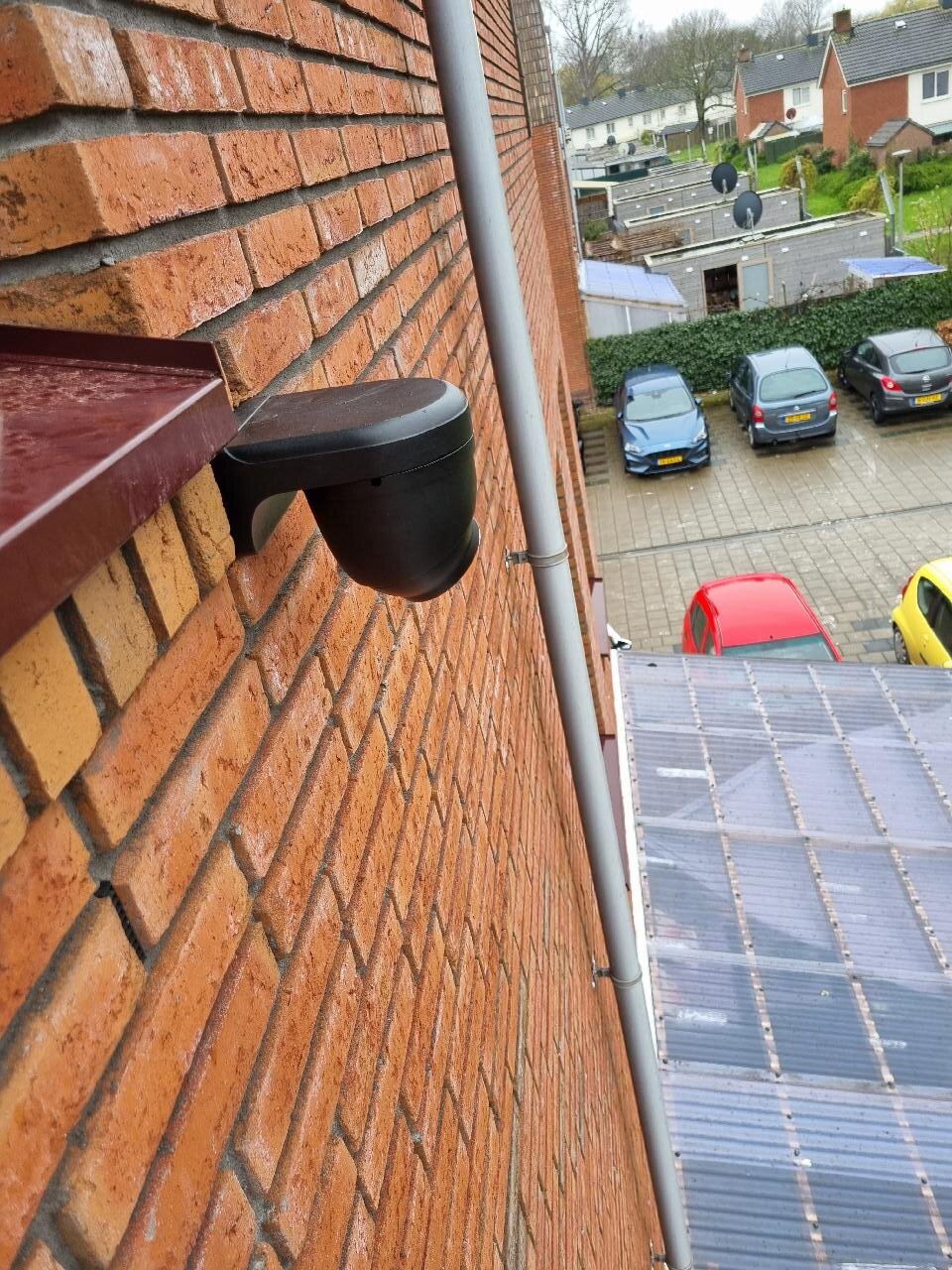 Zwarte turretcamera hoog op de bakstenen gevel, met uitzicht over de parkeerplaats achter de woning