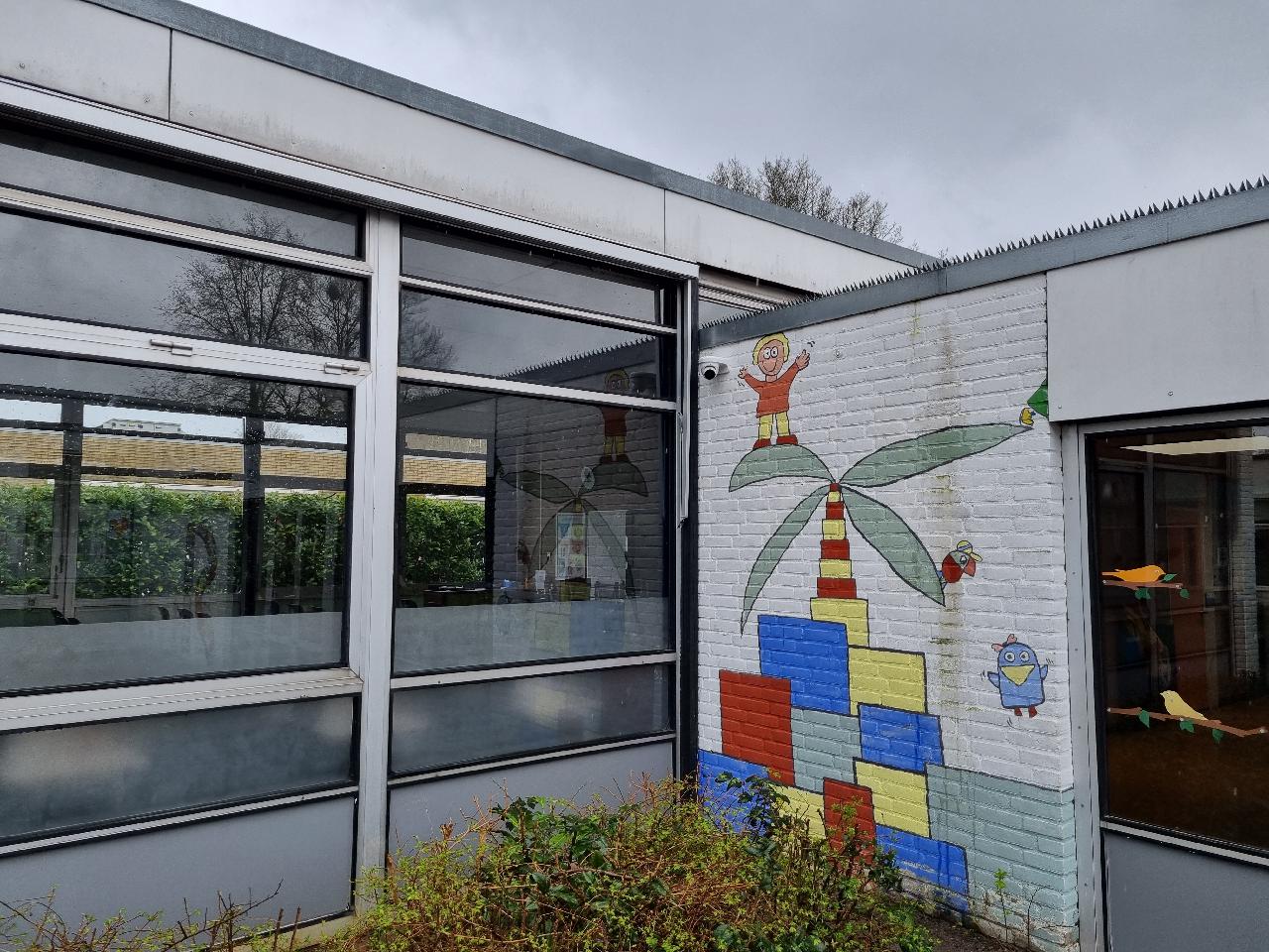 Camera onder de dakrand van een school in Zwolle, naast een muurschildering van een kind en een palmboom