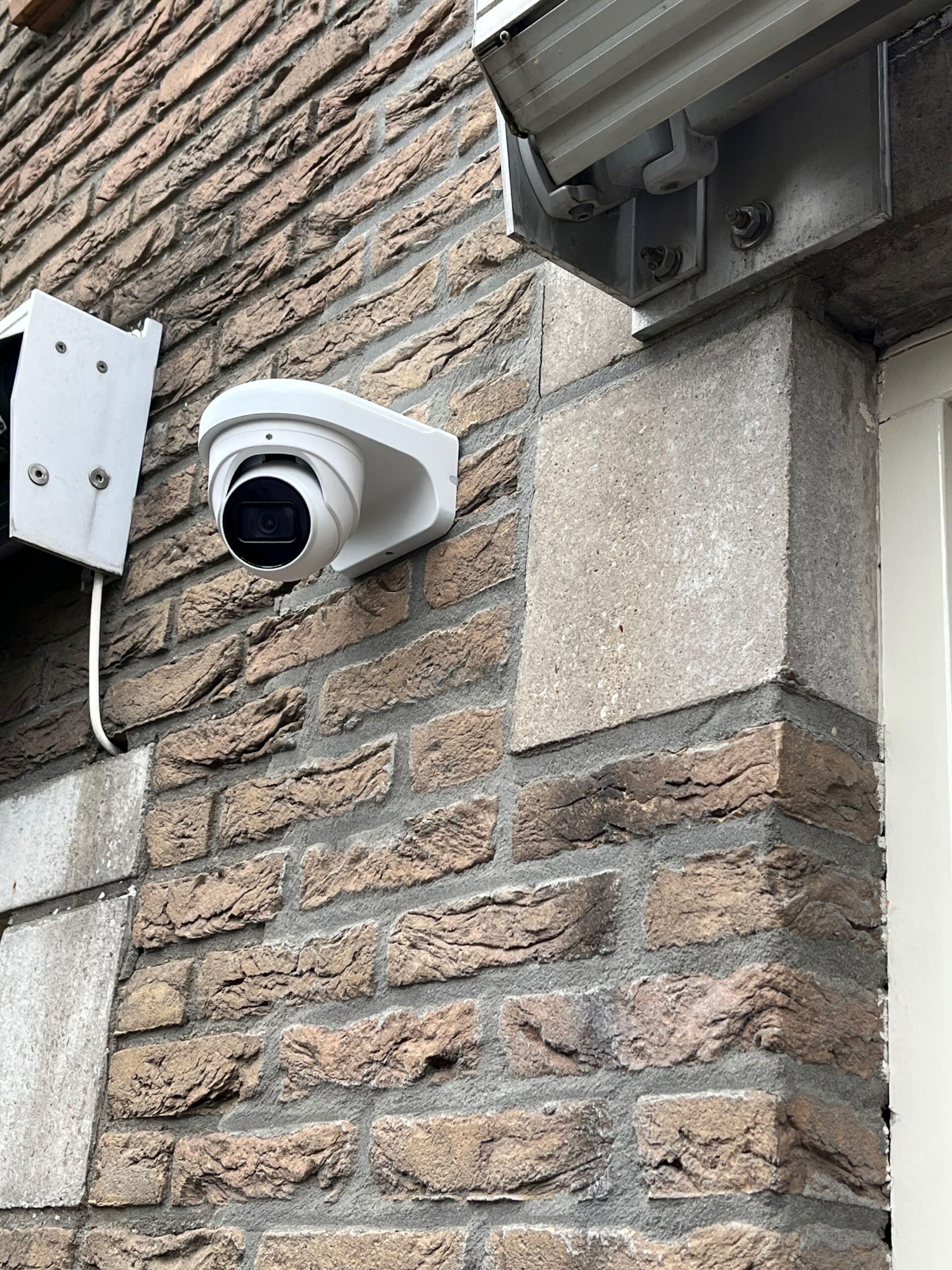 Camera op de gevelhoek onder de dakgoot, naast een bestaand wit wandkastje