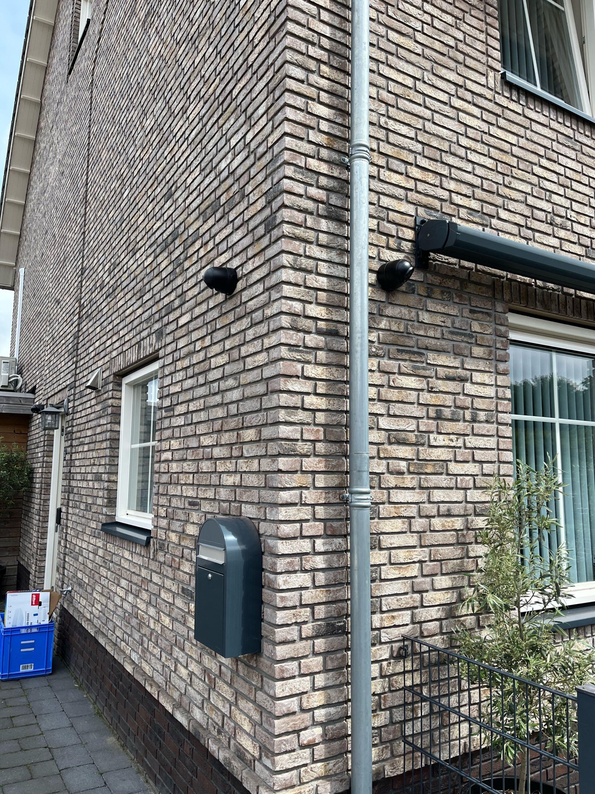 Hoek van een woning met twee zwarte camera's onder de dakrand en een brievenbus aan de gevel