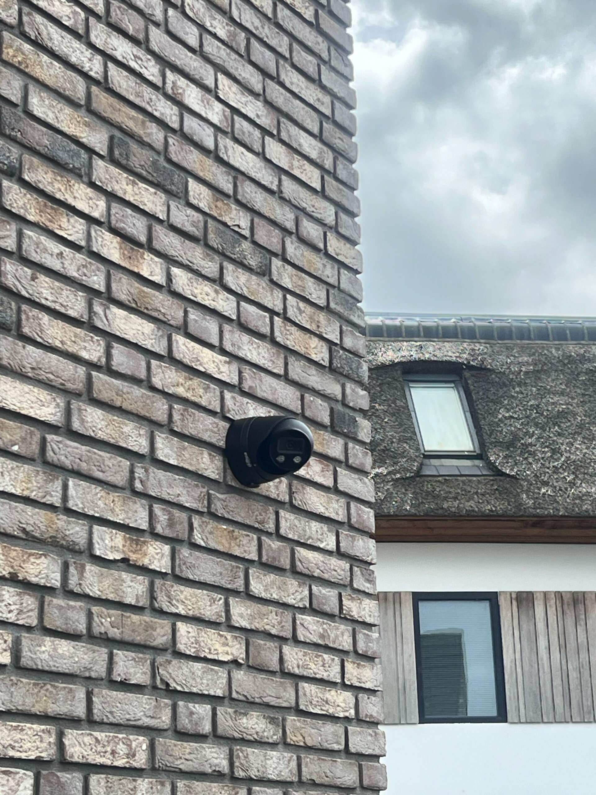 Zwarte camera op de hoek van een woning, met daarachter een rietgedekt dakvlak en een dakraam