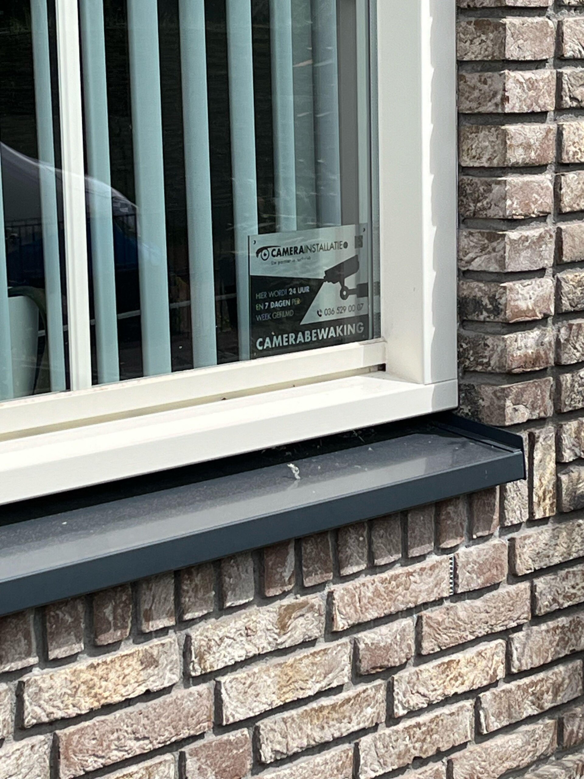 Sticker met de tekst camerabewaking, hier wordt 24 uur en 7 dagen per week gefilmd, geplakt in een raam van de woning