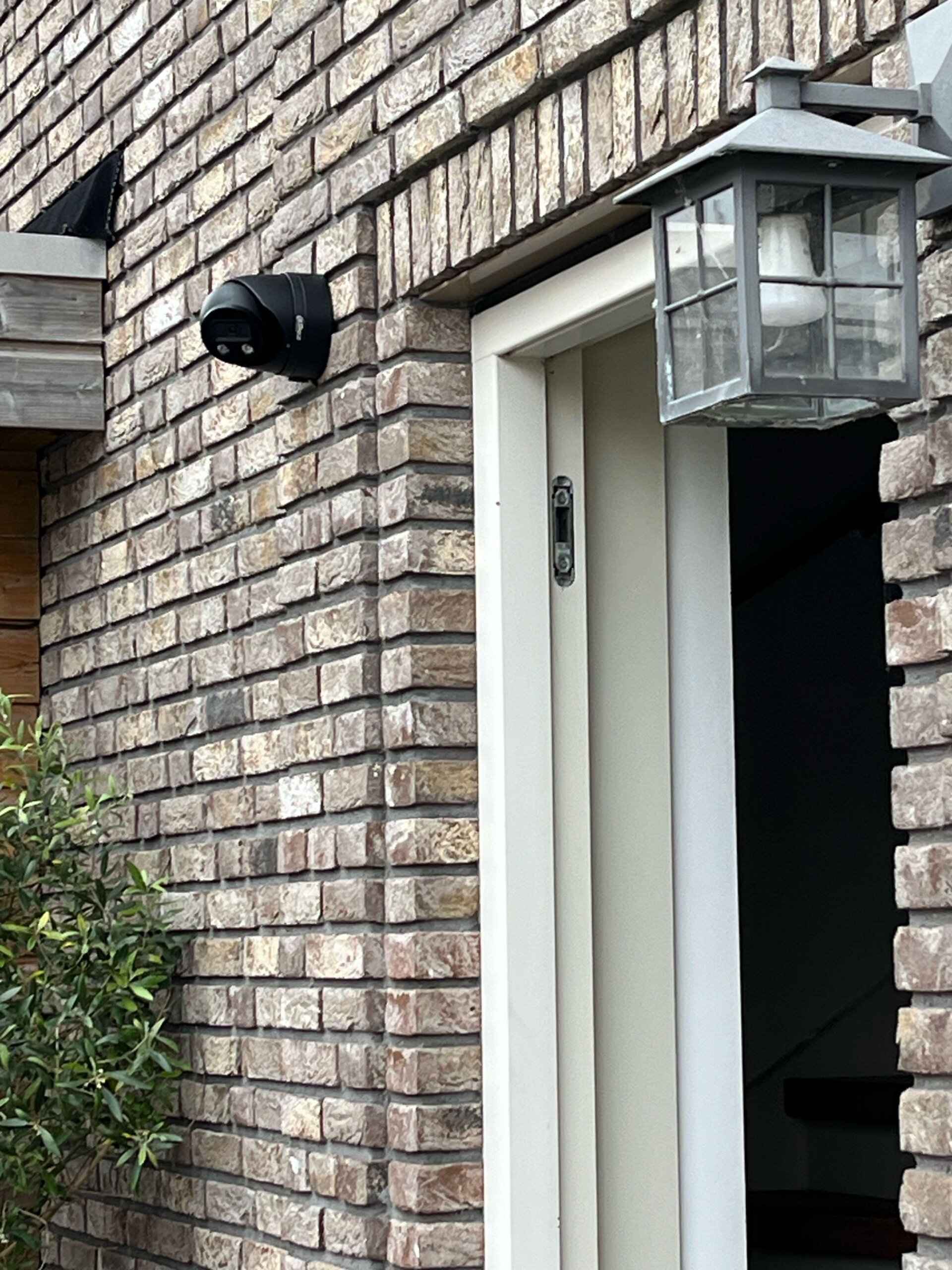 Zwarte camera met ingebouwde verlichting gemonteerd naast de voordeur van een nieuwbouwwoning