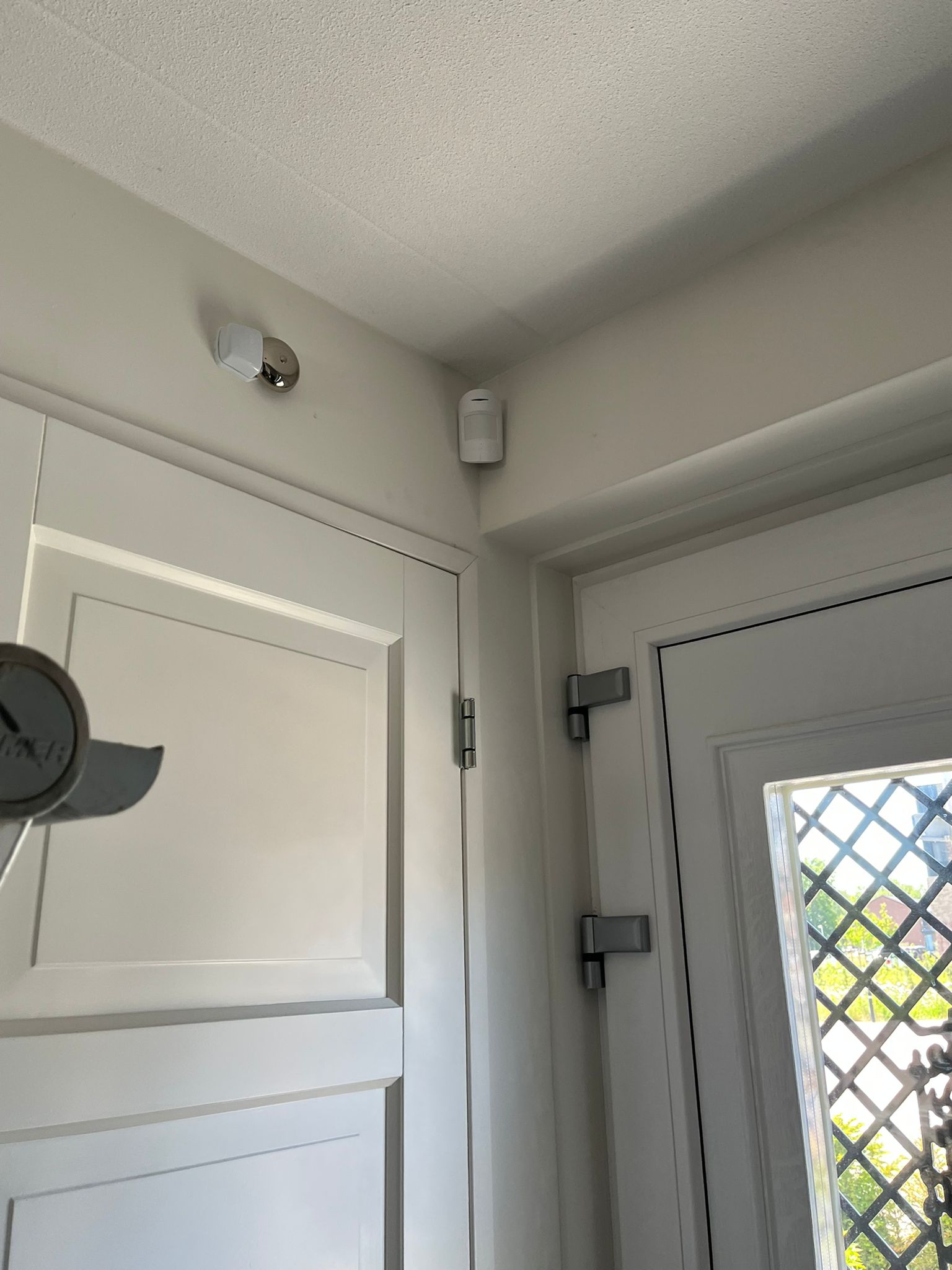 Witte bewegingsmelder van het alarmsysteem, onopvallend hoog in de hoek gemonteerd bij een binnendeur van de woning