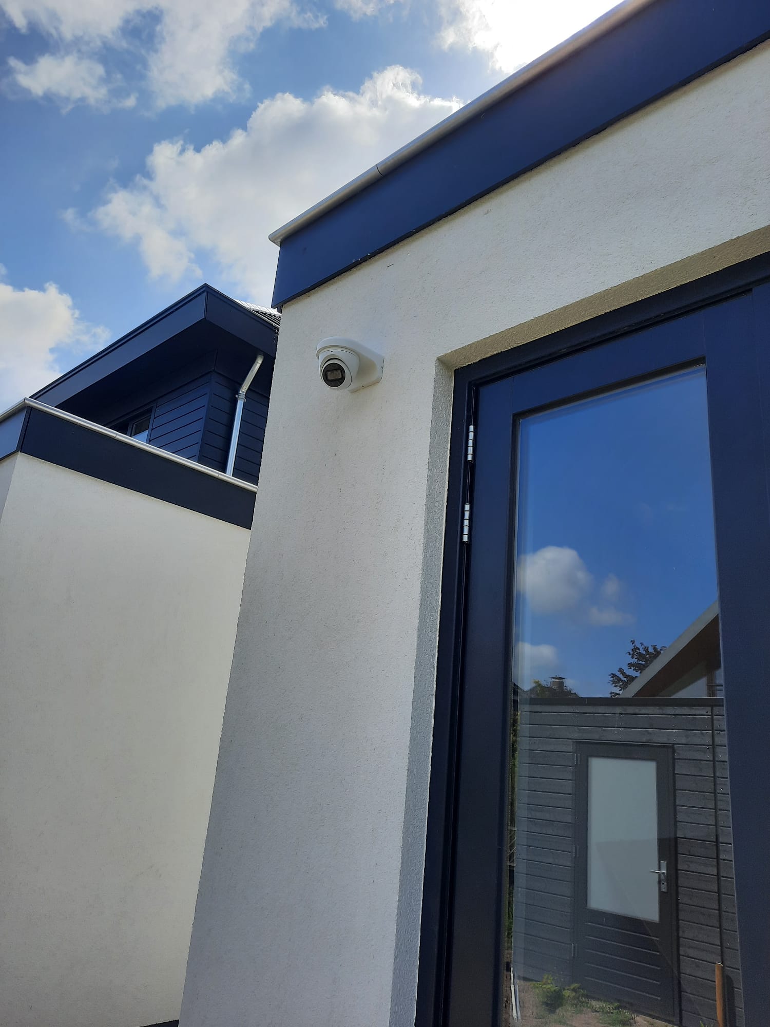 Witte Dahua turret-camera strak gemonteerd hoog op de witgestucte gevel van een moderne nieuwbouwwoning, naast een donkere deur