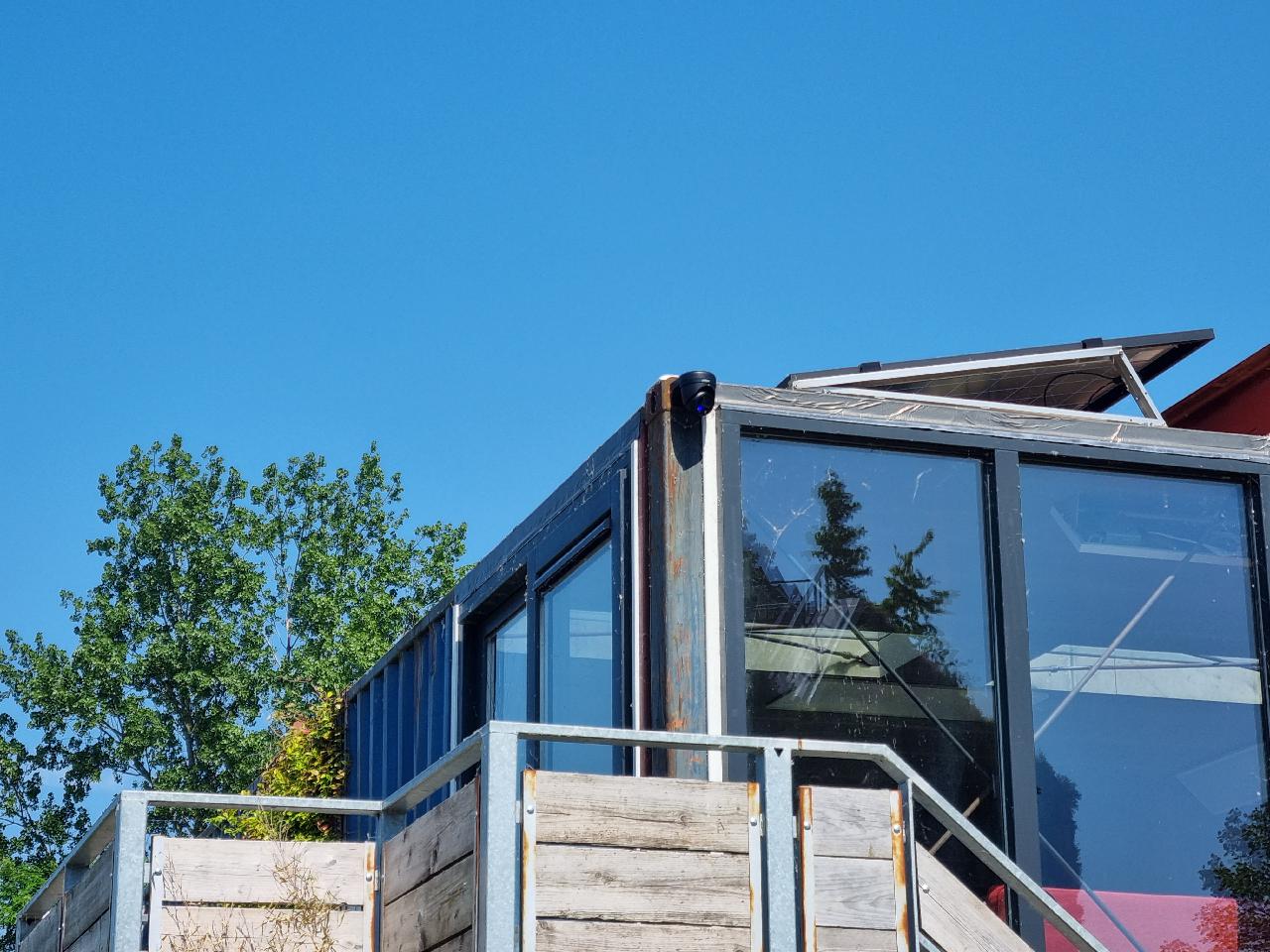 Bewakingscamera hoog op de hoek van een glazen containergebouw met uitzicht over het terras