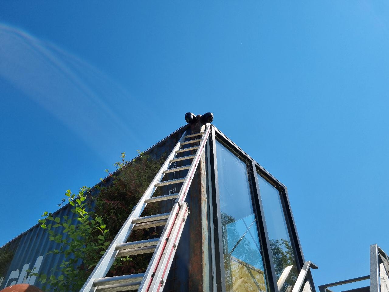 Ladder tegen een container met bovenin een dubbele bewakingscamera tegen een strakblauwe lucht