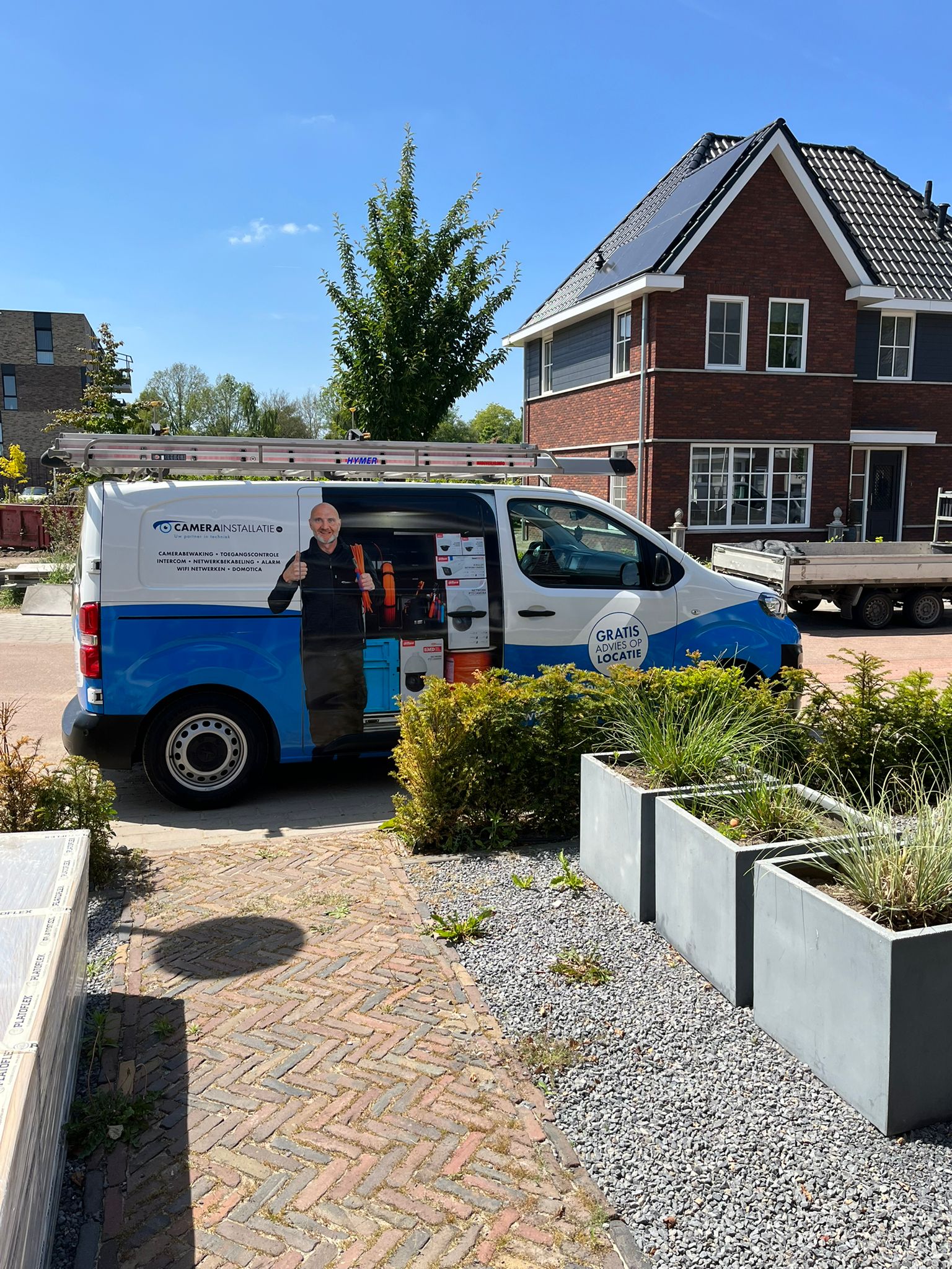 Monteur van CameraInstallatie geeft een duim omhoog bij de herkenbare blauw-witte bedrijfsbus vol gereedschap en Dahua-materiaal, voor een nieuwbouwwoning