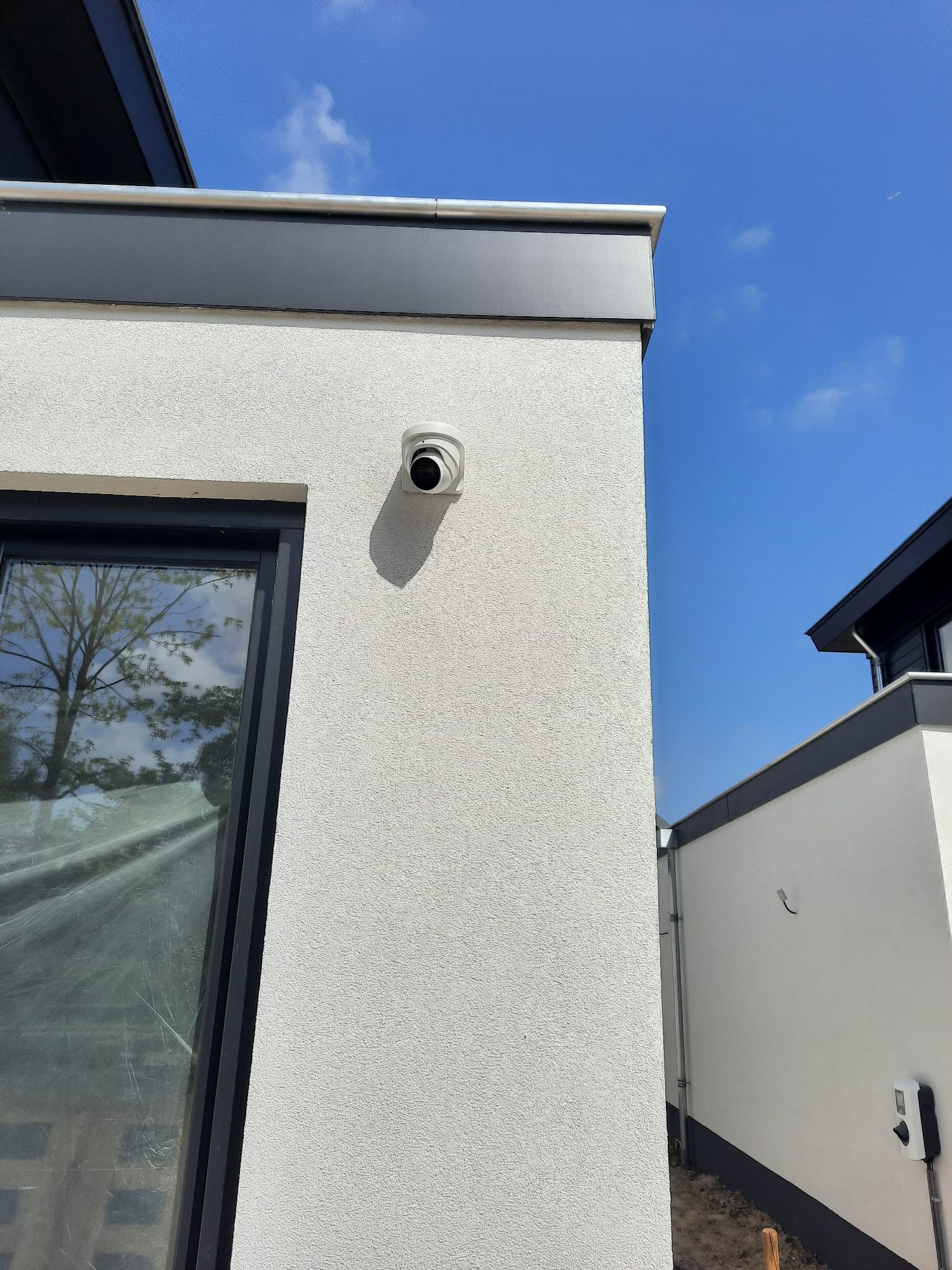 Witte Dahua turret-camera op de hoek van een witgestucte moderne nieuwbouwwoning tegen een strakblauwe lucht