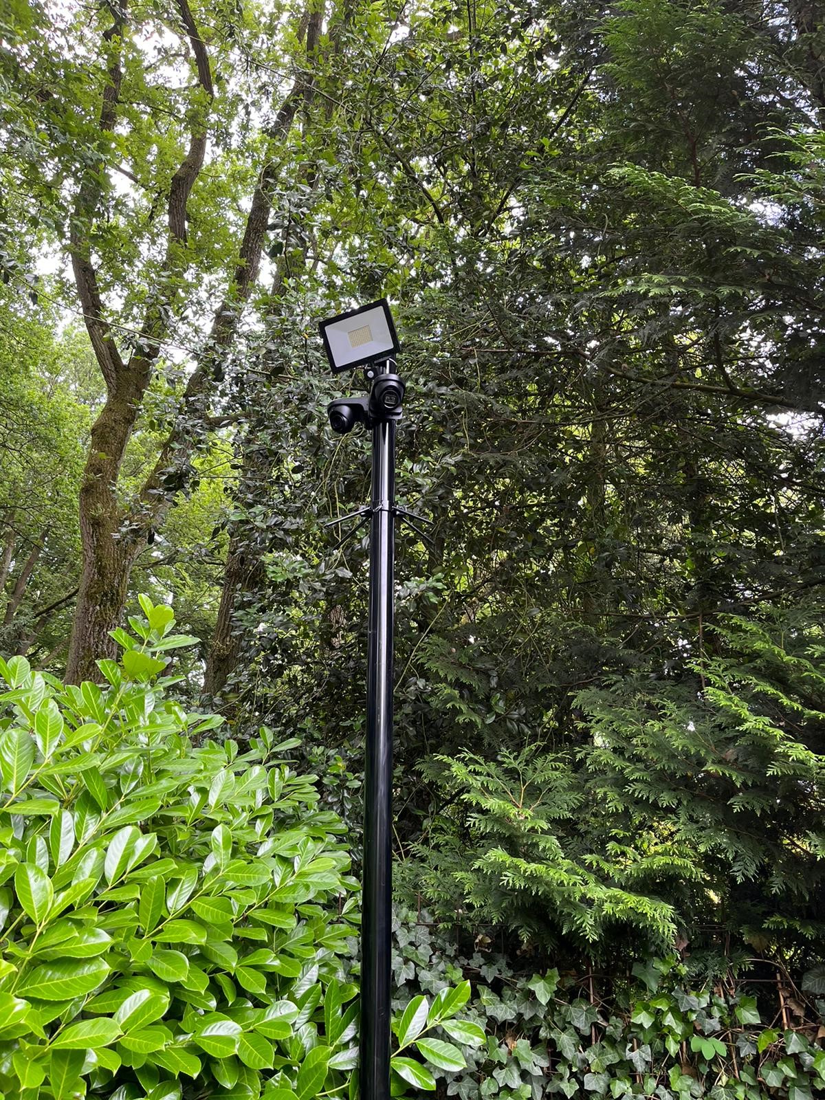 Slanke zwarte mast met een camera erop, uitstekend boven dicht groen