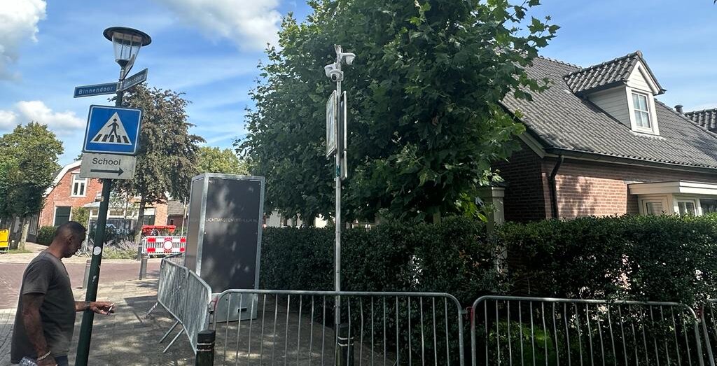 Tijdelijke camera op een verplaatsbare paal met bouwhekken langs een straat bij een schoolzone