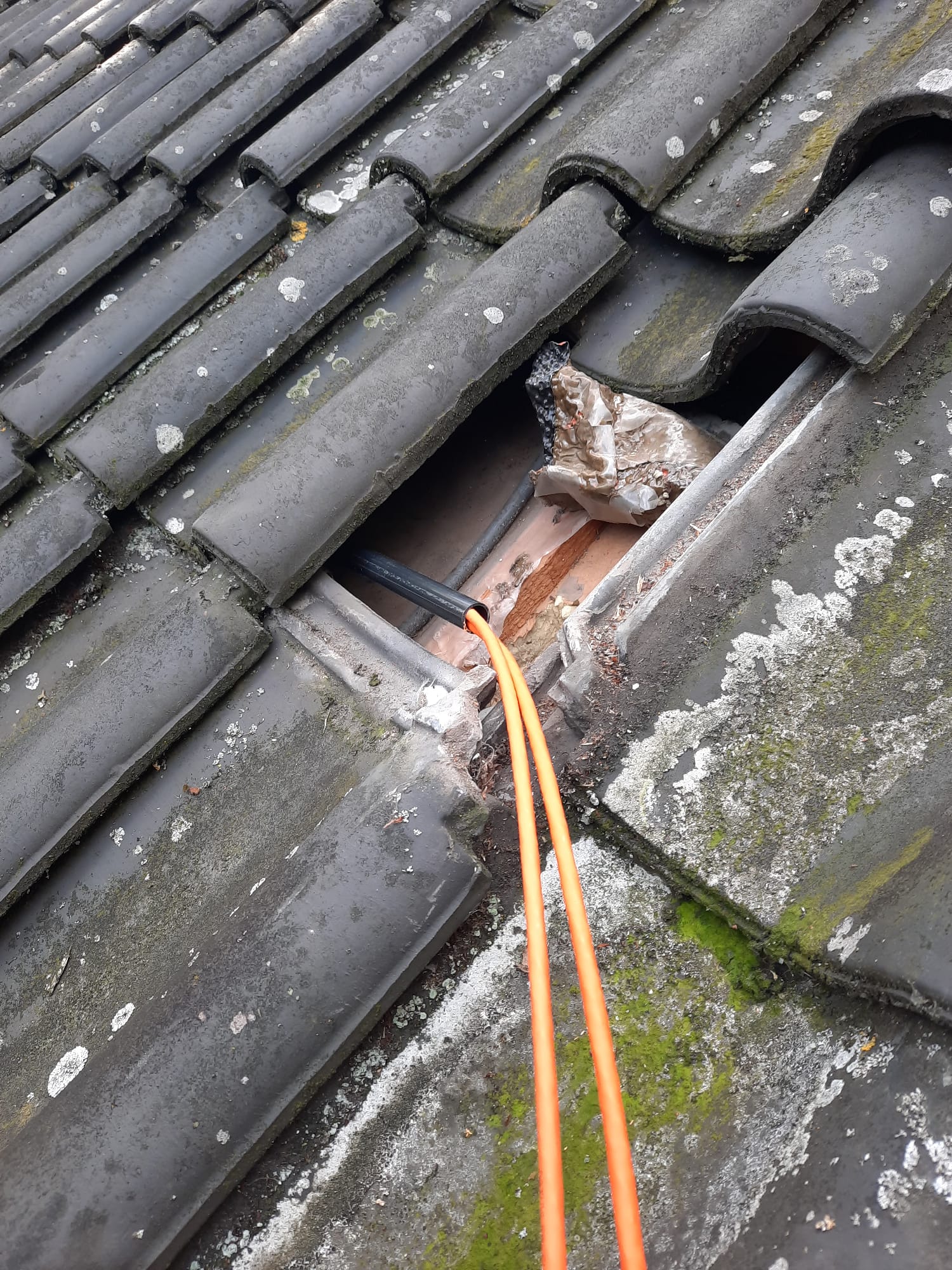 Oranje netwerkkabel wordt netjes onder de dakpannen door getrokken tijdens de installatie