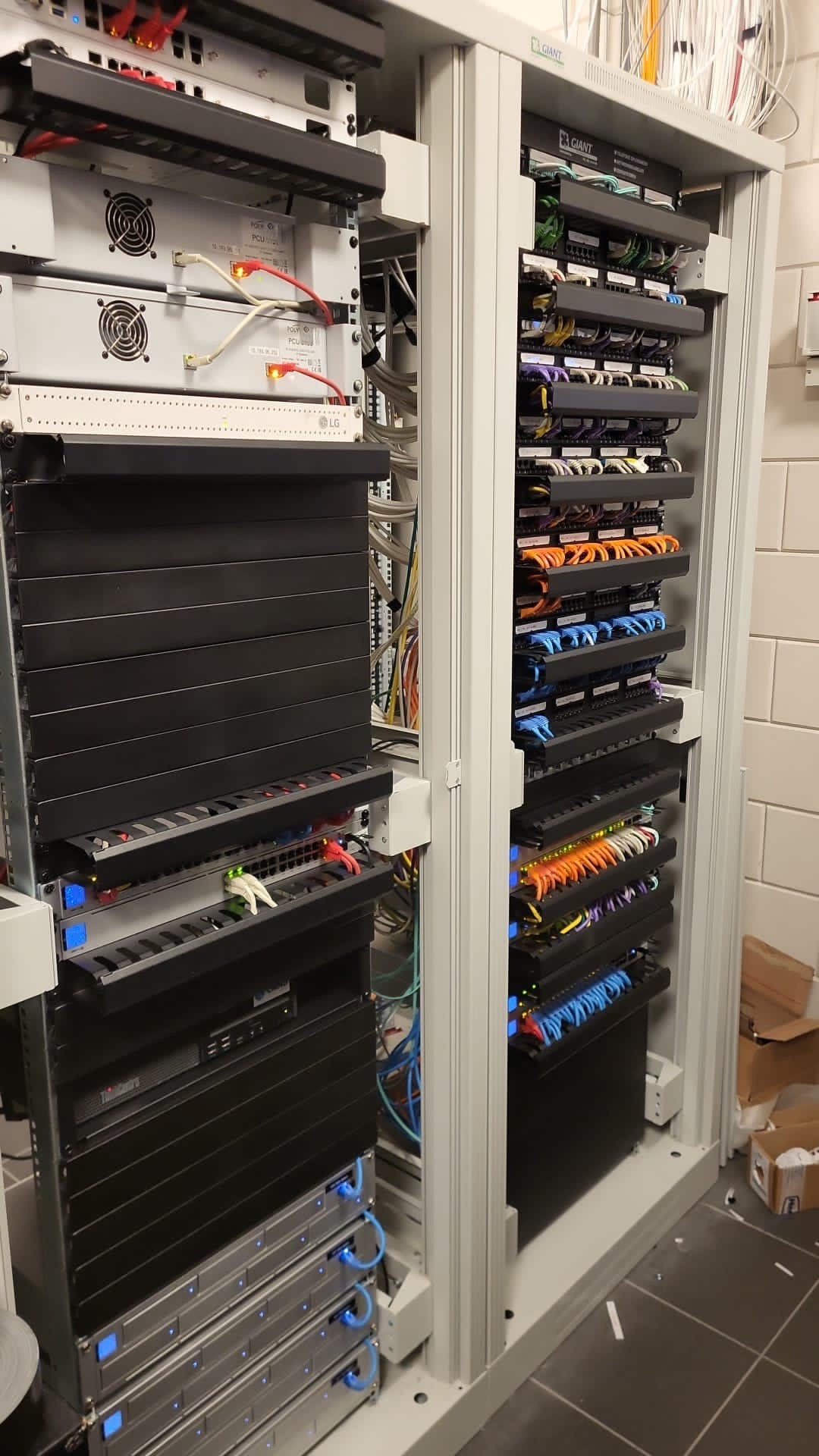 Netwerkkast met meerdere patchpanelen en kleurgecodeerde bekabeling: oranje, blauw, groen en paars netjes gerangschikt