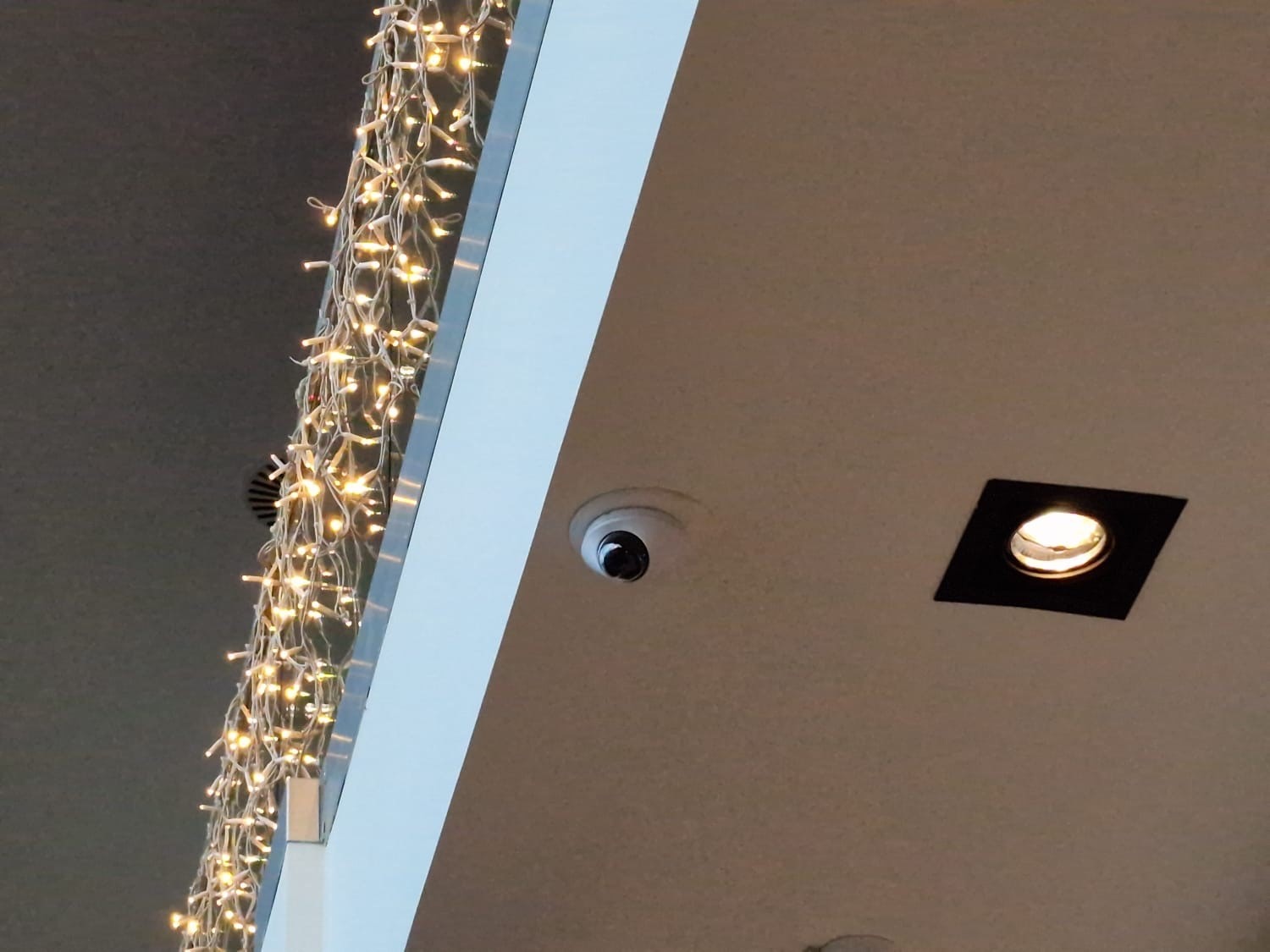 Kleine witte dome-camera weggewerkt in een plafond, naast een inbouwspot en een lichtsnoer