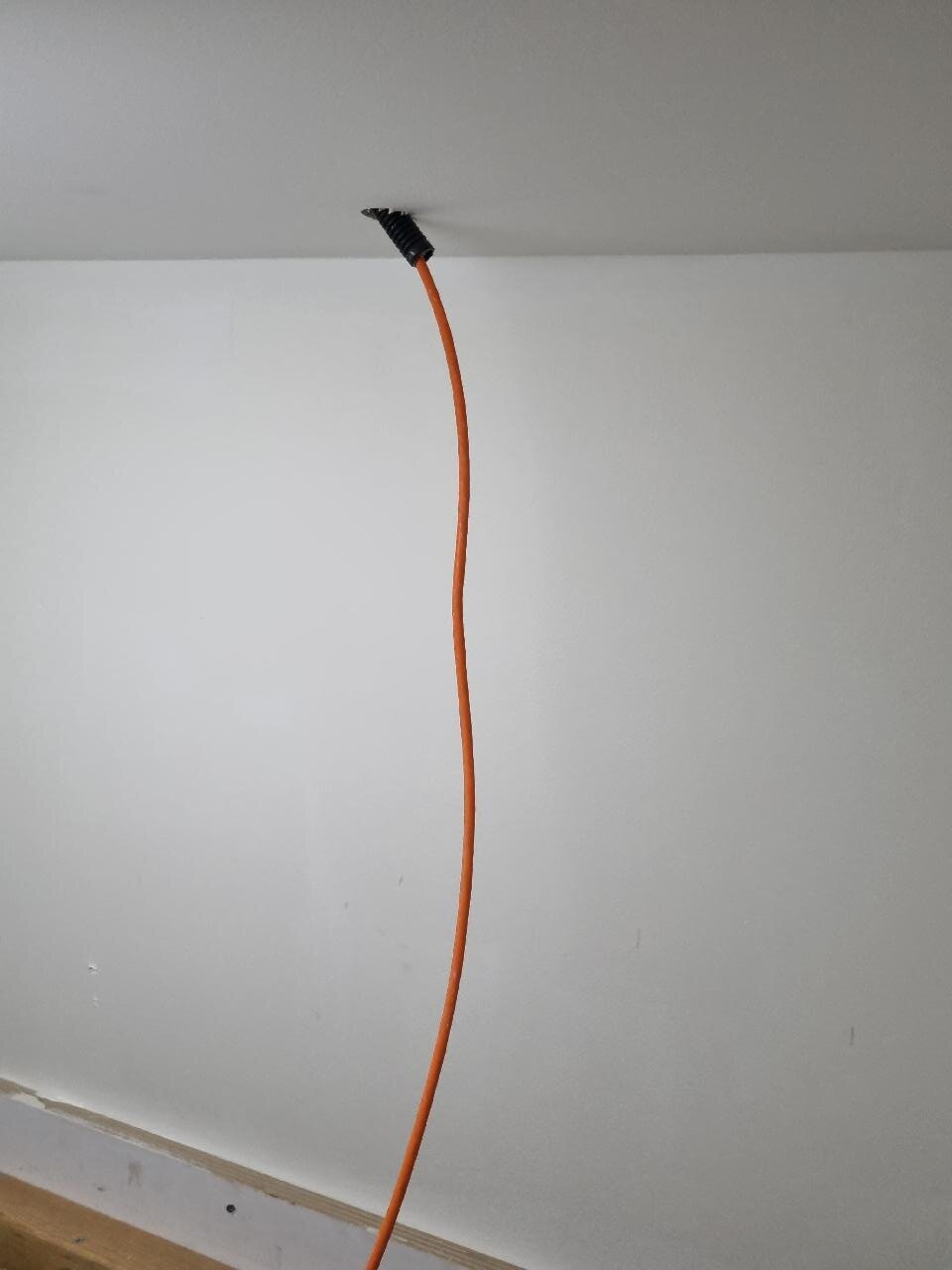 Enkele oranje netwerkkabel die netjes uit een doorvoertule in een wit plafond komt