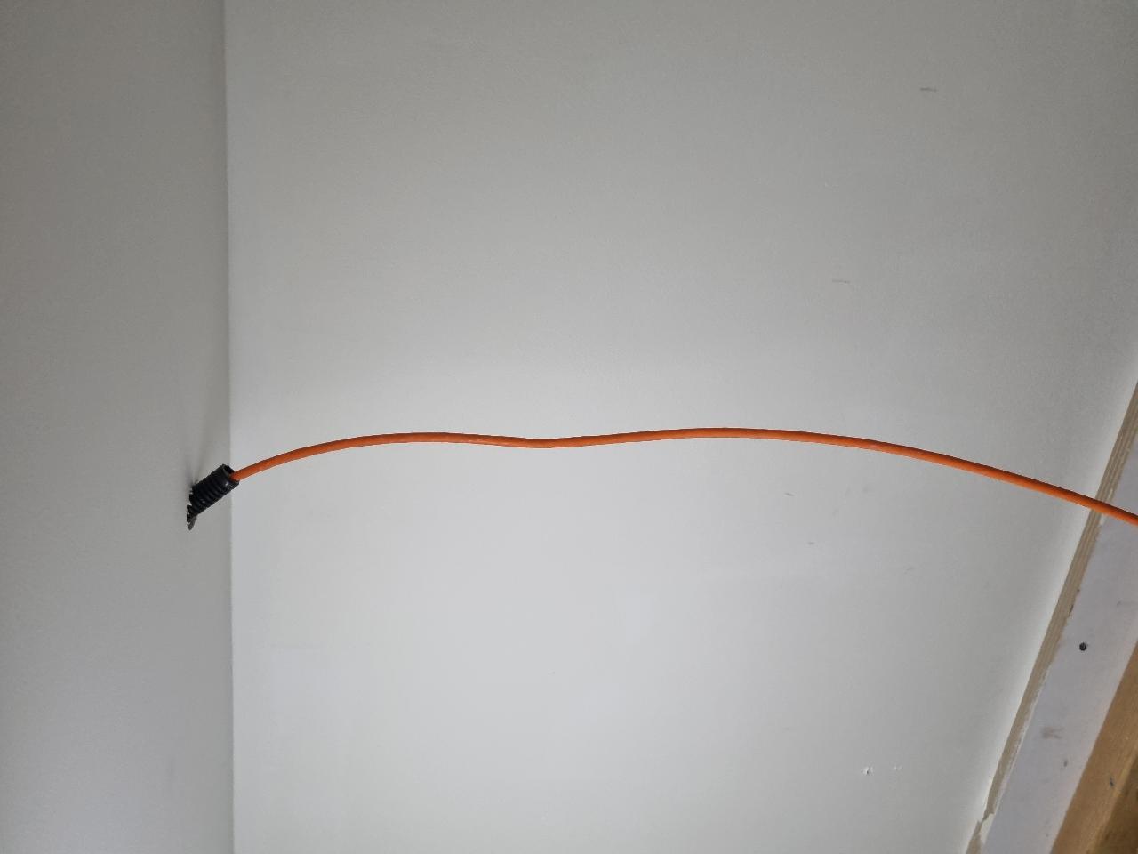 Enkele oranje netwerkkabel die netjes uit het plafond langs een witte wand naar beneden loopt