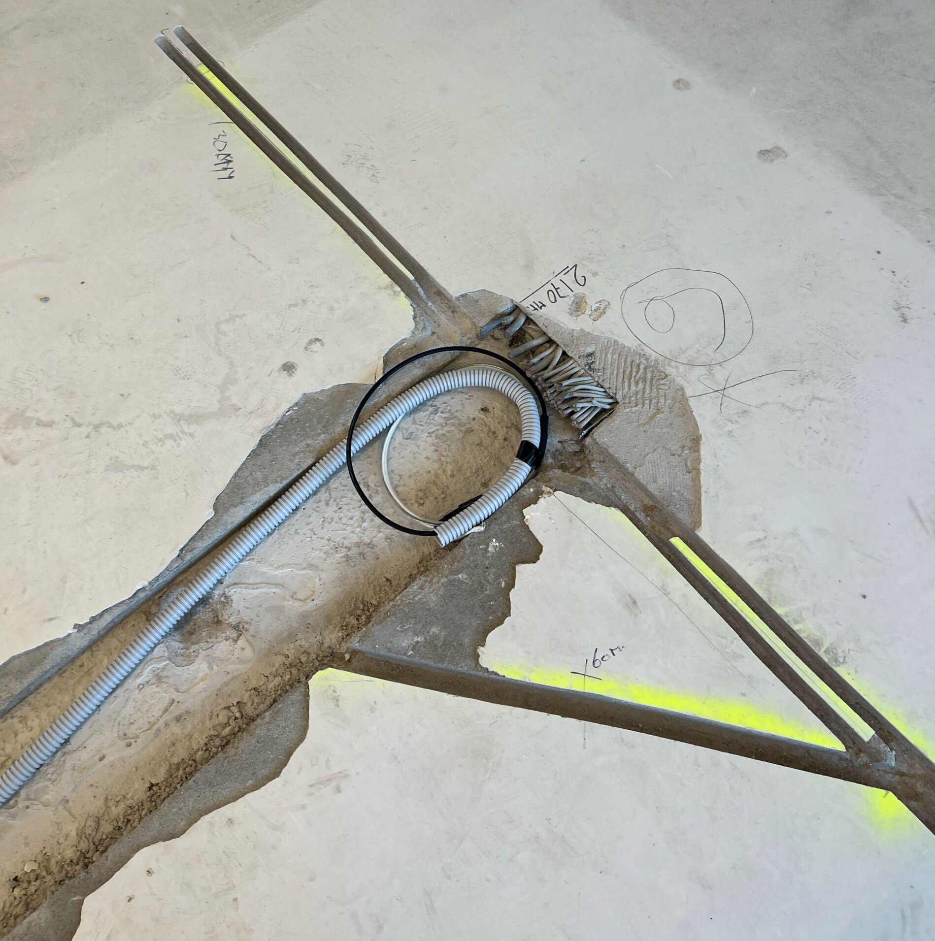In een betonvloer gefreesde sleuven met een flexibele kabelbuis, met handgeschreven maatvoering in centimeters ernaast