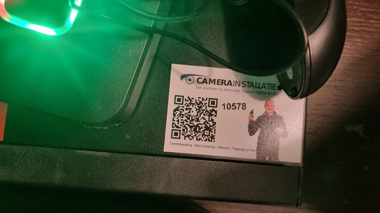 Servicesticker van CameraInstallatie met QR-code en systeemnummer, geplakt op de recorder met groene statusled