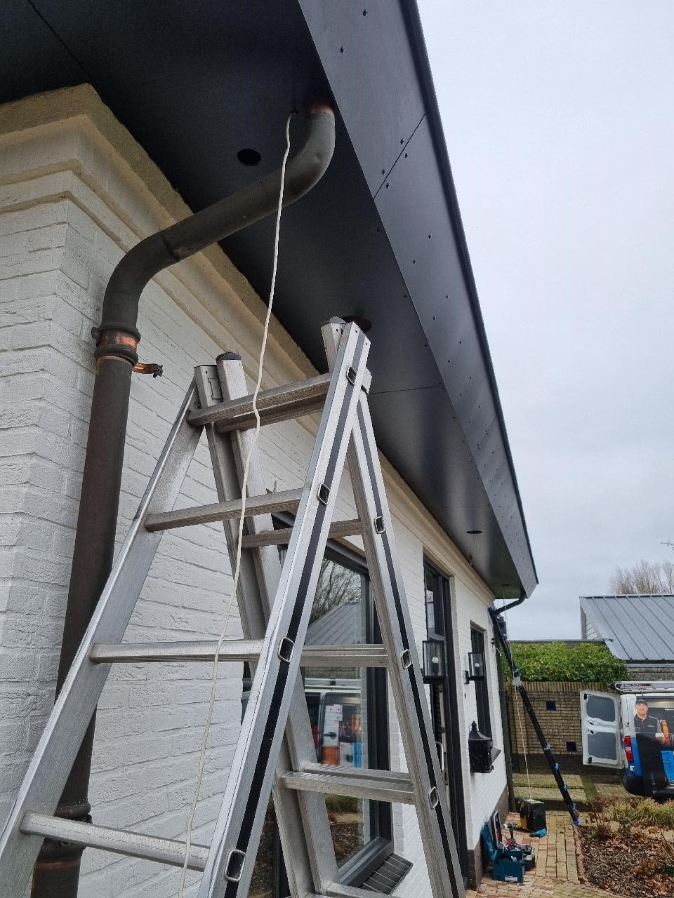 Boring in het zwarte boeideel van de woning met een witte trekdraad die naar beneden hangt, ladder ernaast