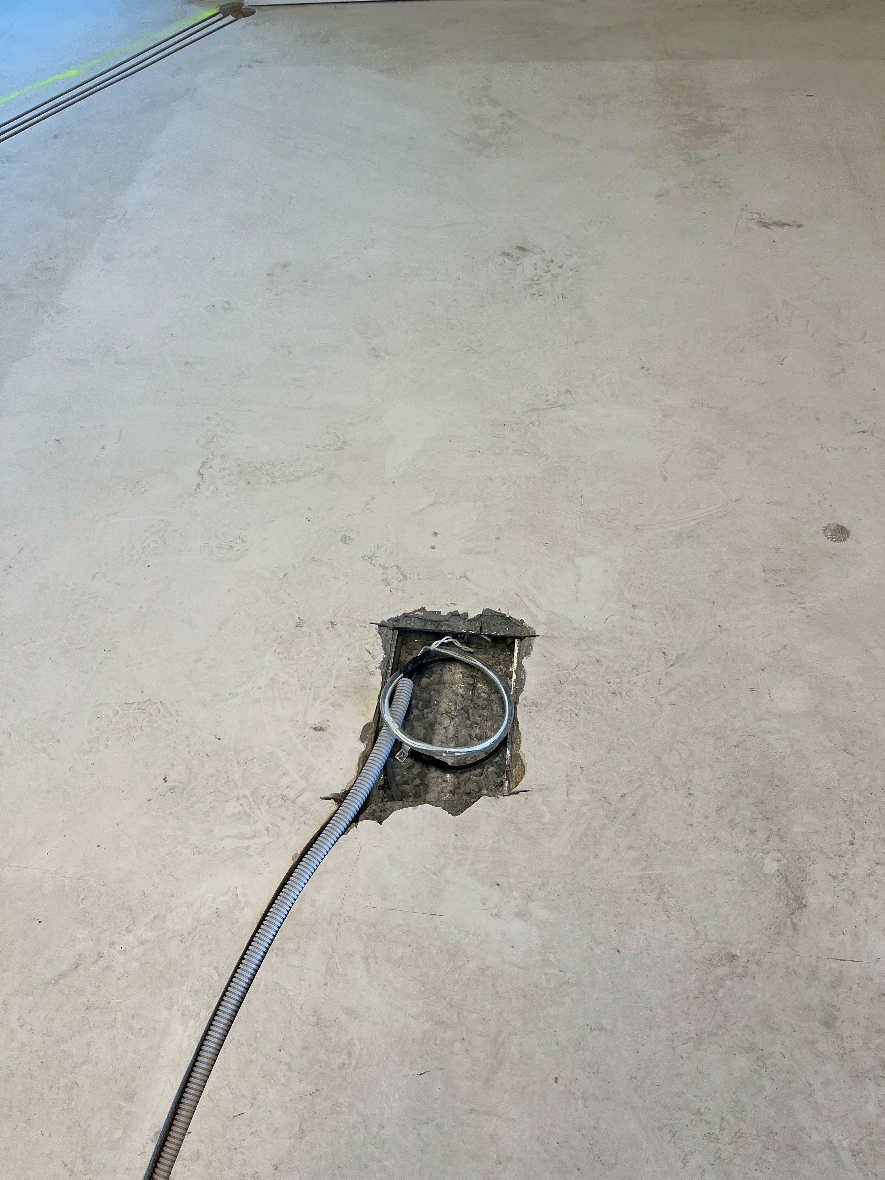 Uitsparing in een betonvloer met een opgerolde netwerkkabel en kabelbuis, klaar om afgewerkt te worden tot vloerpot