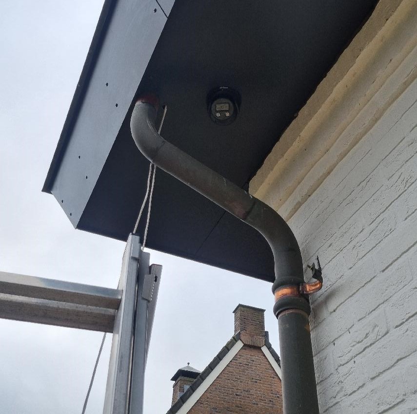 Close-up van de zwarte turret-camera die vlak in het zwarte boeideel van de woning is gemonteerd, naast de regenpijp