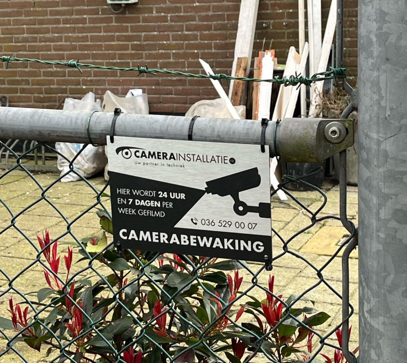Bordje van CameraInstallatie aan een gaashek met de tekst hier wordt 24 uur en 7 dagen per week gefilmd