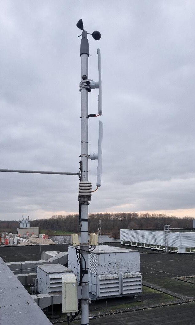 Hoge mast op een dak met twee straalzender-antennes, een PoE-injector en bekabeling die naar beneden loopt