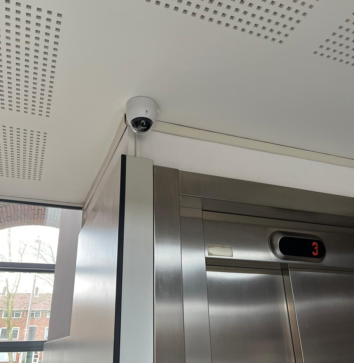 Witte dome-camera aan het plafond boven de roestvrijstalen liftdeuren in de hal van een appartementencomplex