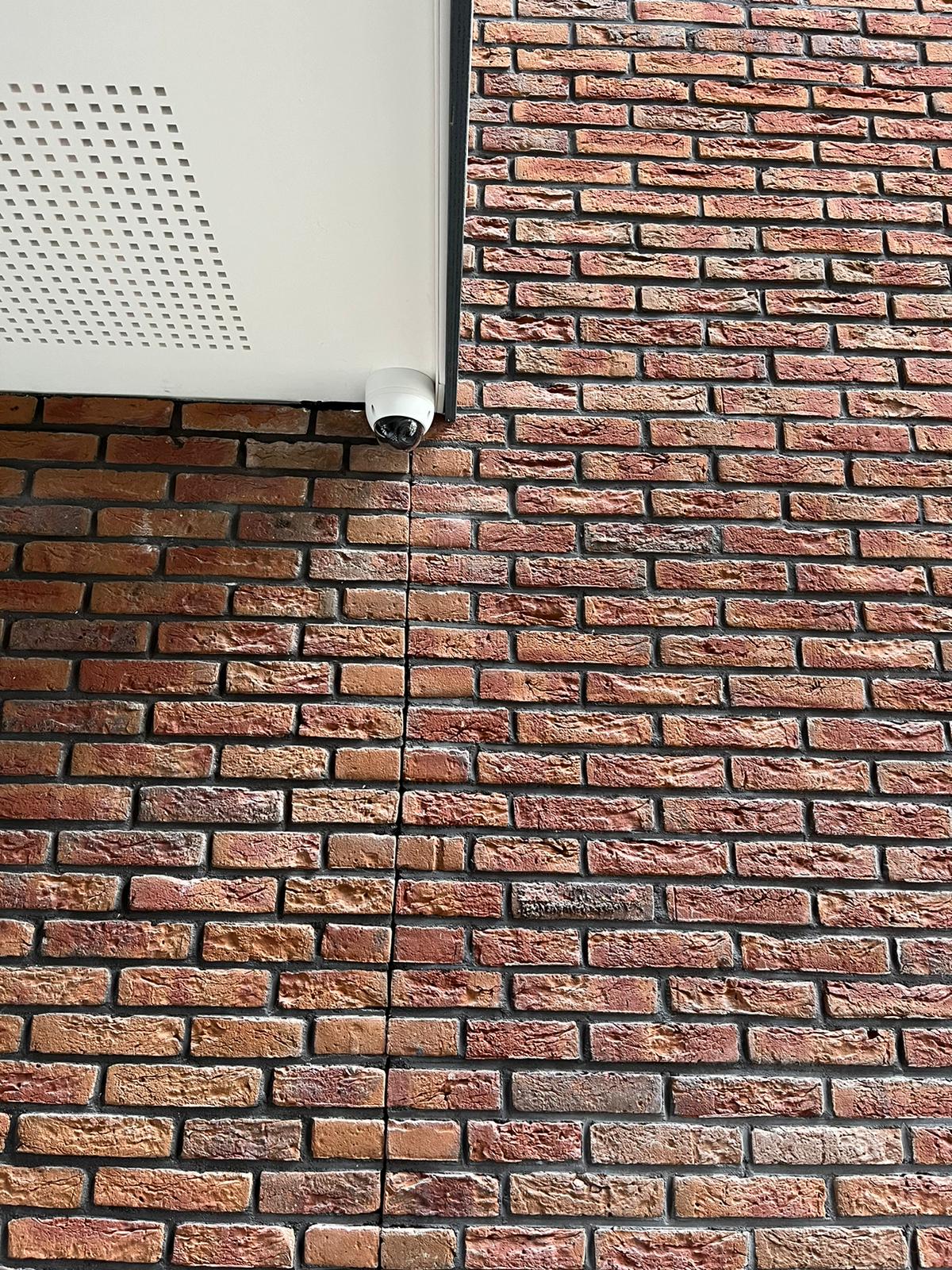 Witte dome-camera op de hoek van een bakstenen gevel, vlak onder de rand van een luifel