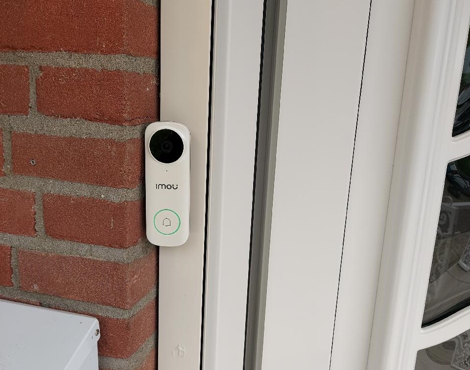 Digitale deurbel met camera gemonteerd op het kozijn naast de voordeur van de woning, met verlichte belknop