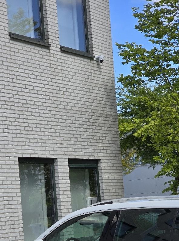 Witte dome-camera onder een raam op een lichte bakstenen gevel van een bedrijfspand