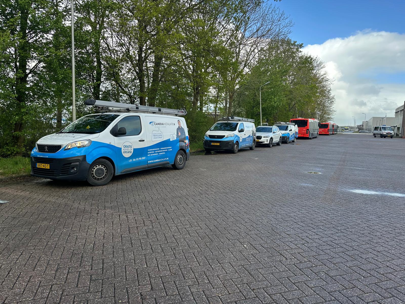 Twee bedrijfsbussen van CameraInstallatie geparkeerd op het terrein naast een rij lijnbussen
