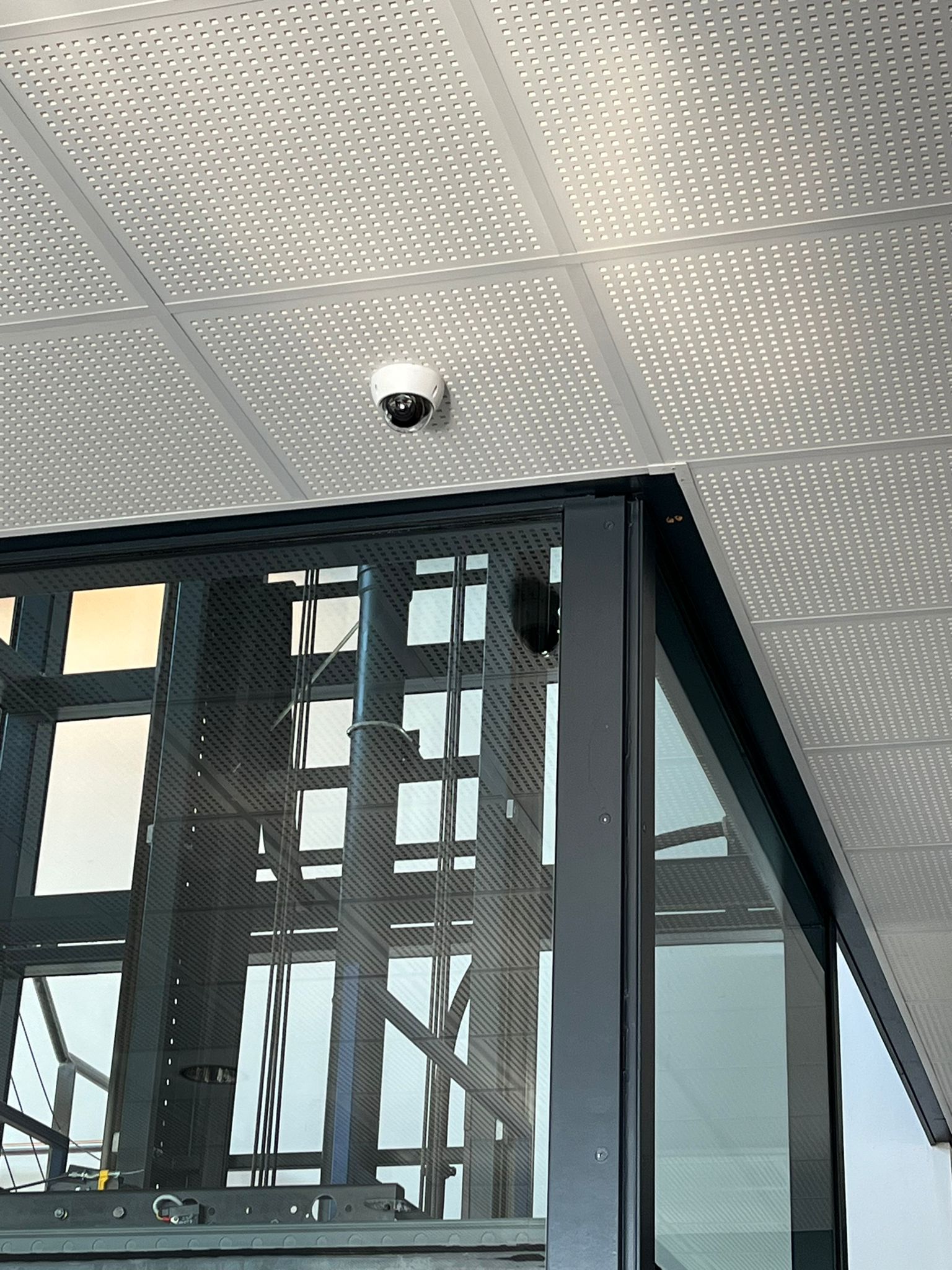 Witte dome-camera in een systeemplafond boven de glazen schacht van een lift in een appartementencomplex