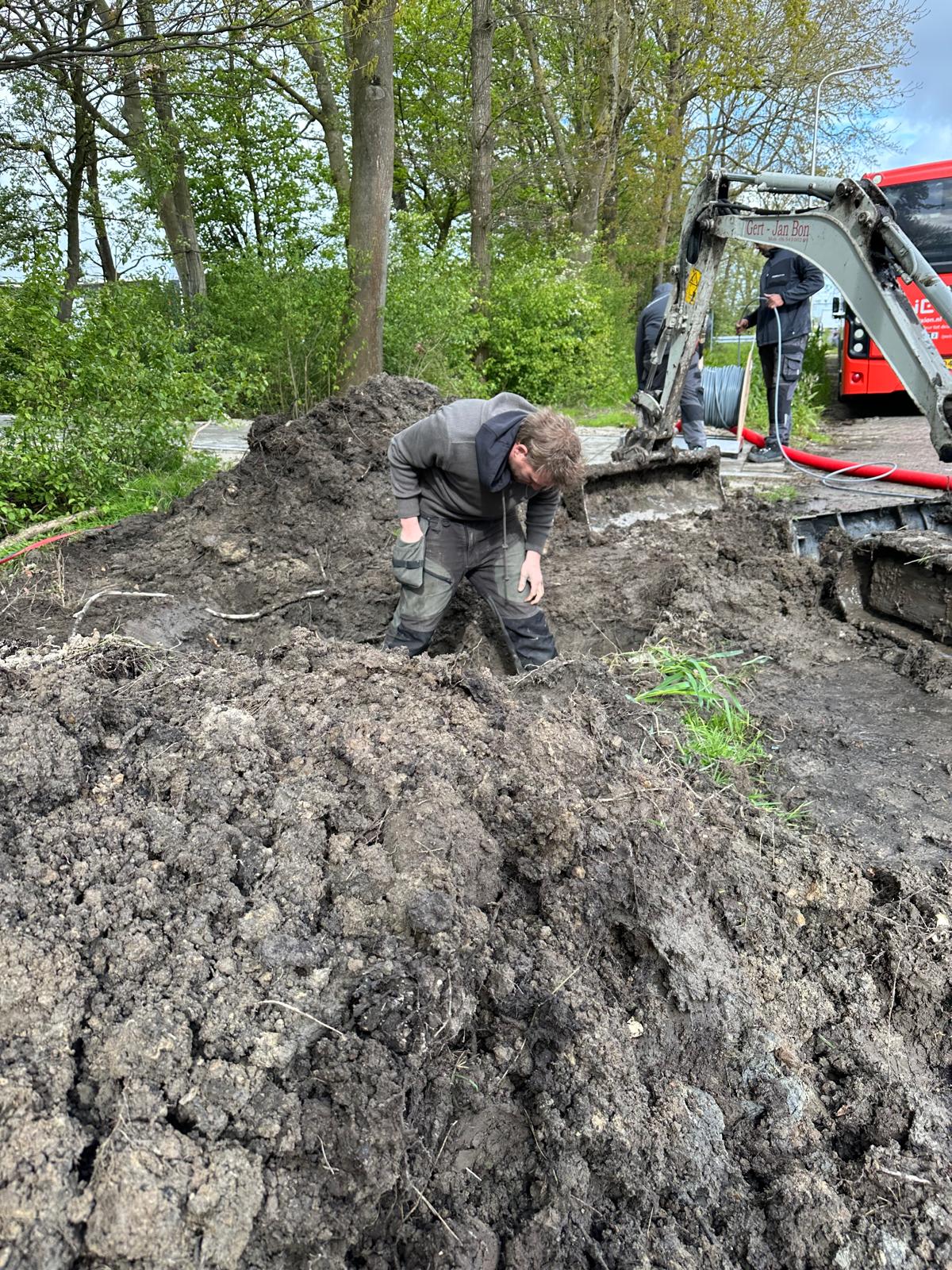 Monteur van CameraInstallatie werkt in een diepe, modderige sleuf naast de rupsbanden van een minigraver