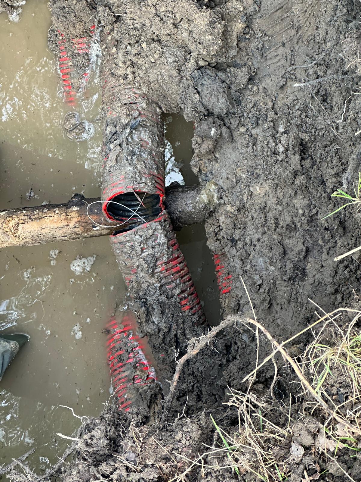 Close-up in de sleuf van een opengewerkte rode mantelbuis met de zwarte kabel er zichtbaar in
