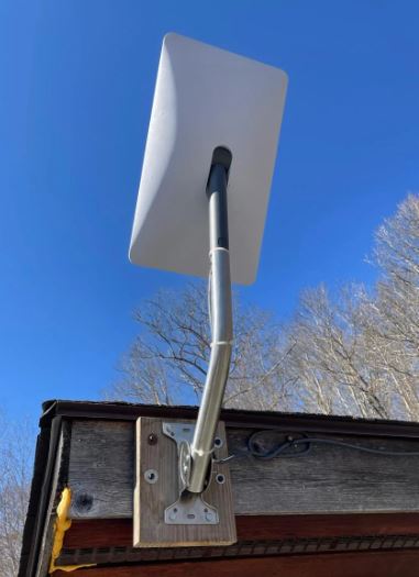 Satellietschotel op een stalen beugel die met een houten montageplaat op een gevelrand is bevestigd, kabel netjes langs de rand geleid