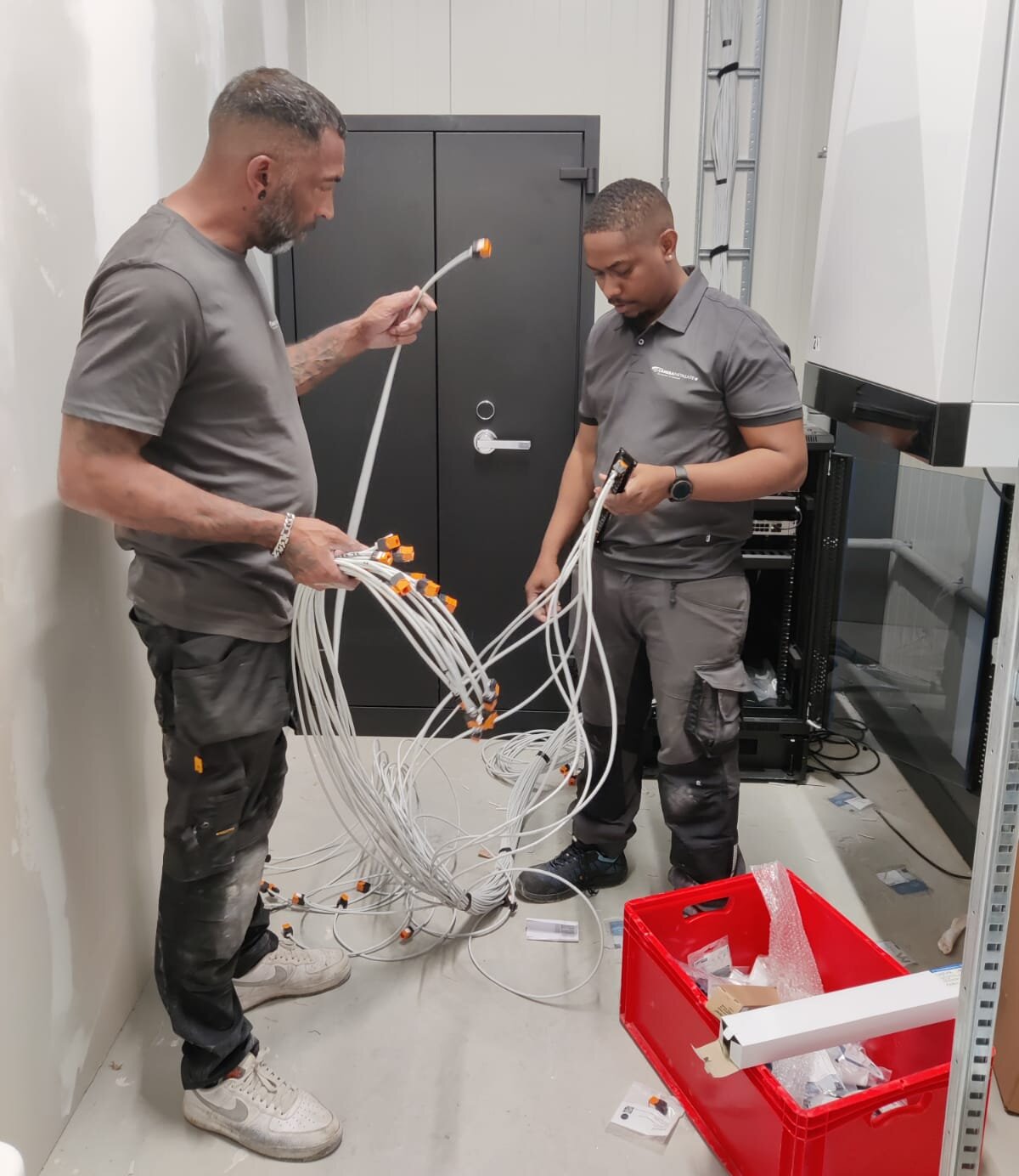 Twee monteurs van CameraInstallatie sorteren in een technische ruimte een bundel netwerkkabels met oranje connectoren