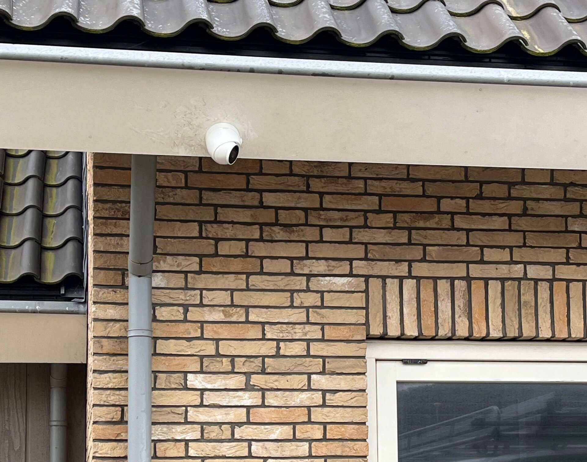 Witte dome-camera onder de dakoverstek van een bakstenen gebouw, met de kabel onzichtbaar weggewerkt