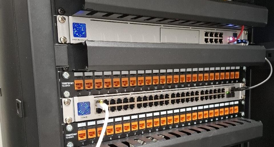 Patchkast met twee 24-poorts patchpanelen met oranje keystones en een netwerkswitch met aangesloten patchkabels