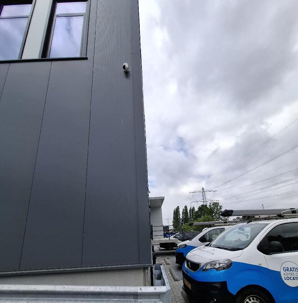 Camera op de hoek van een bedrijfspand met twee bedrijfsbussen van CameraInstallatie op het parkeerterrein