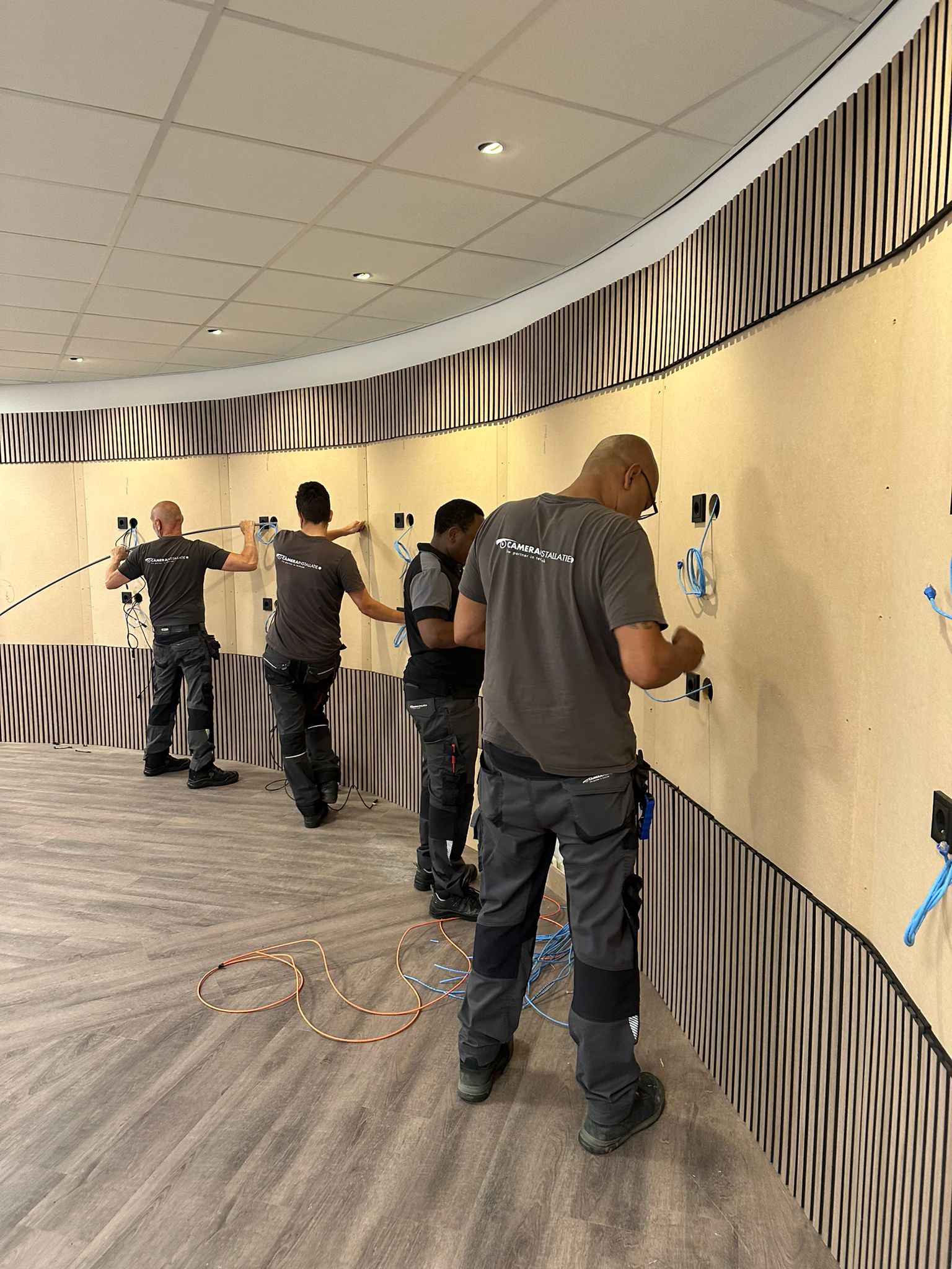 Vier monteurs van CameraInstallatie trekken samen netwerkkabels langs de gebogen lamellenwand