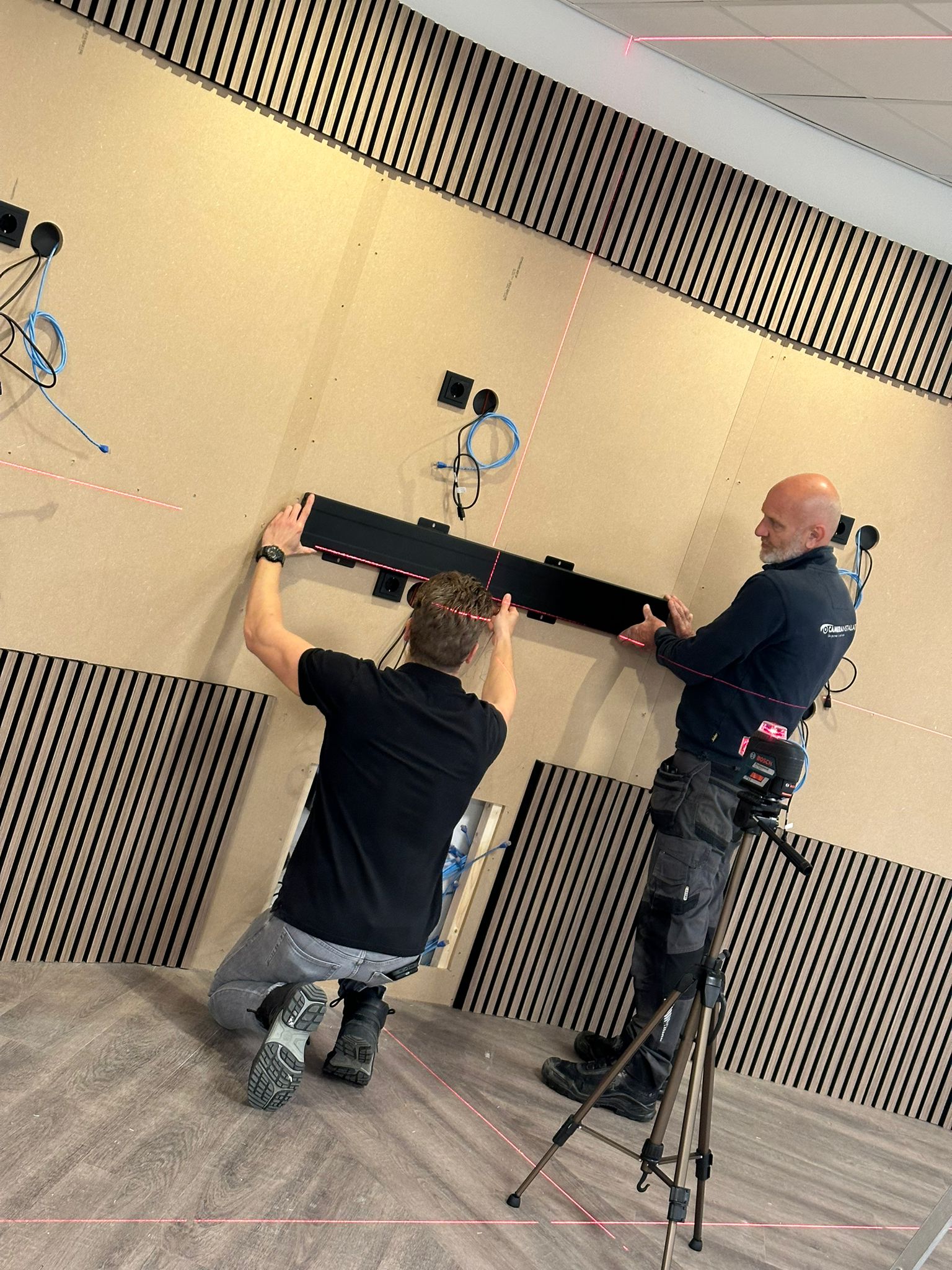 Twee monteurs van CameraInstallatie monteren met een laserwaterpas een beugelrail voor de schermpanelen