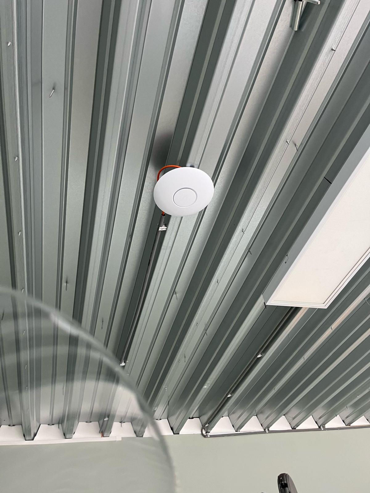 Access point tegen het stalen dakbeschot van een magazijn, met de oranje kabel eraan