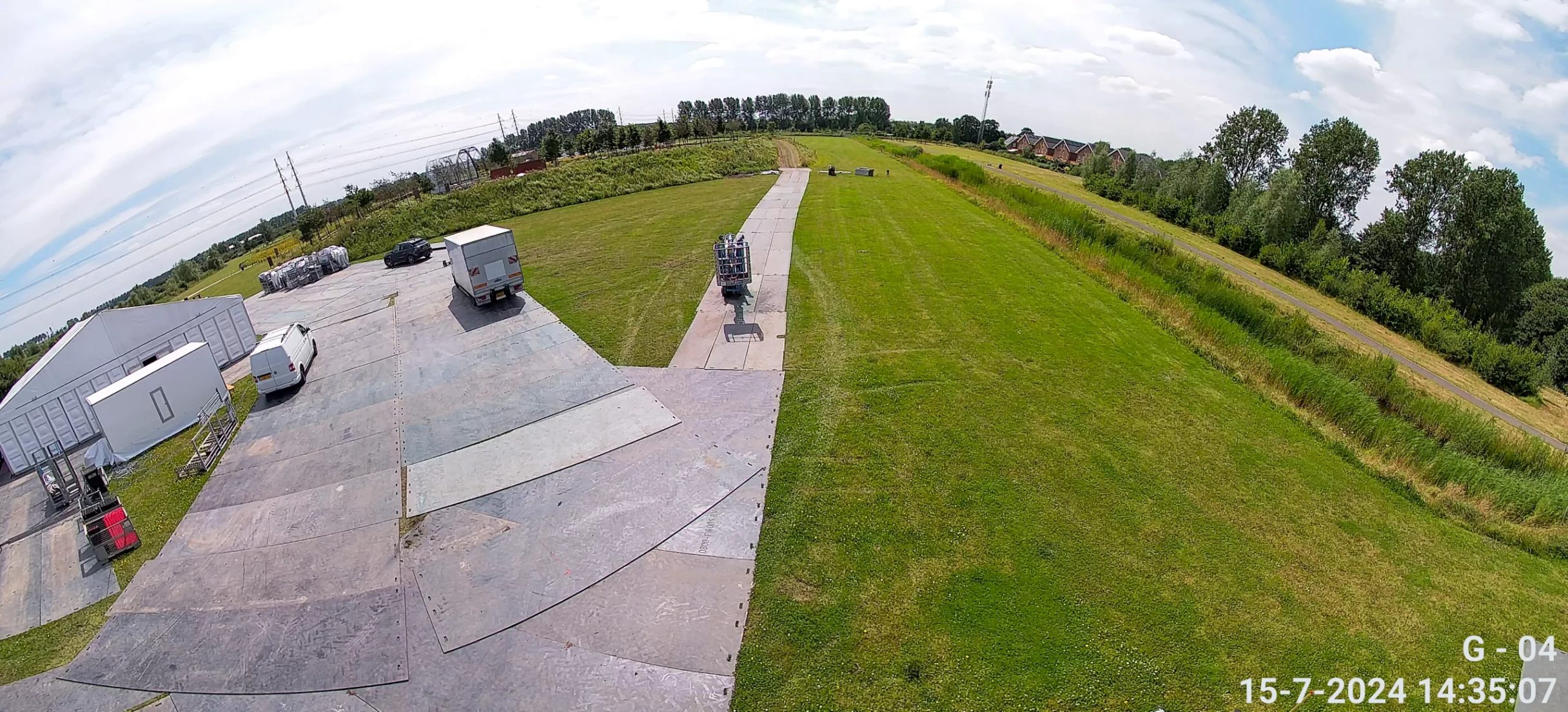 Camerabeeld vanaf een mast over een verhard rijplaatvlak met een vrachtwagen, een bestelbus en aangevoerd materieel