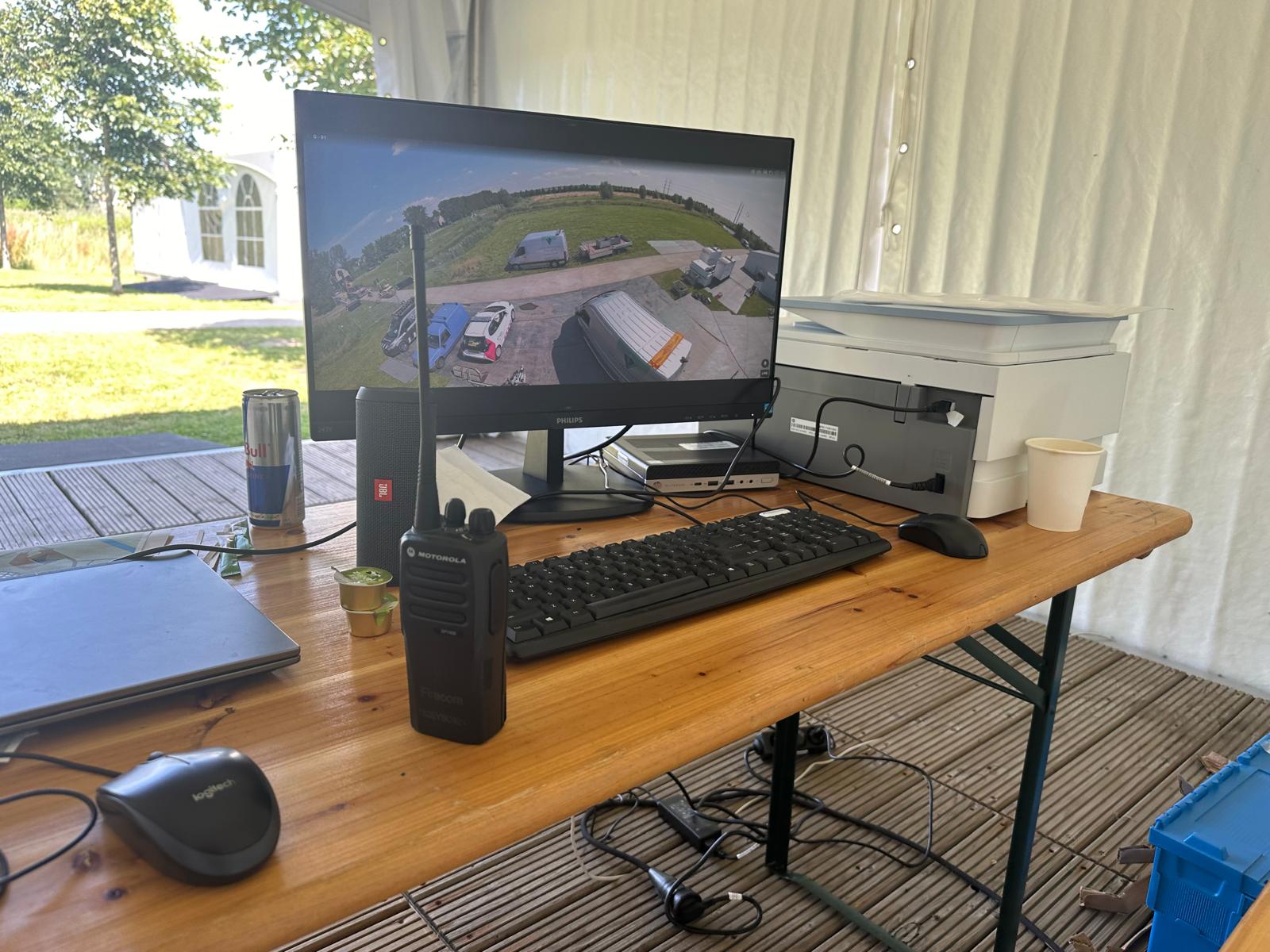 Scherm met live camerabeelden van een buitenterrein, naast een portofoon op een werktafel
