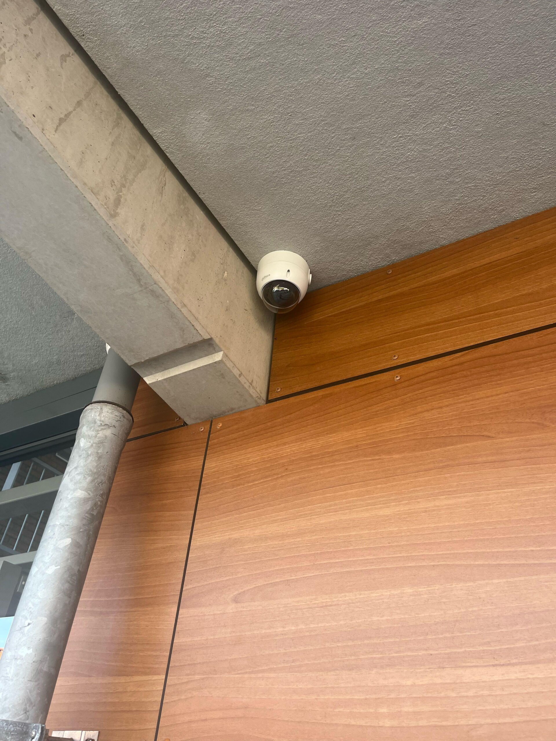 Witte dome-camera van Dahua gemonteerd in de hoek tussen een betonnen plafond en houten gevelbekleding