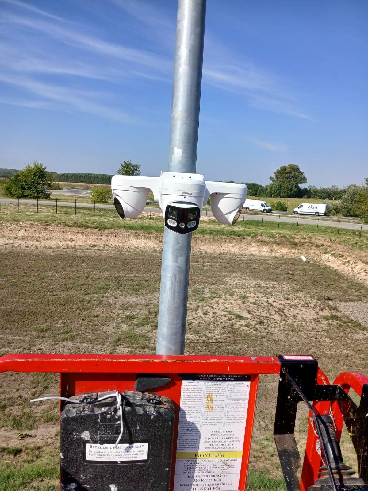 Camerapaal met drie camera's die uitkijken over een weg waar bestelbussen passeren, gefotografeerd vanuit een hoogwerker