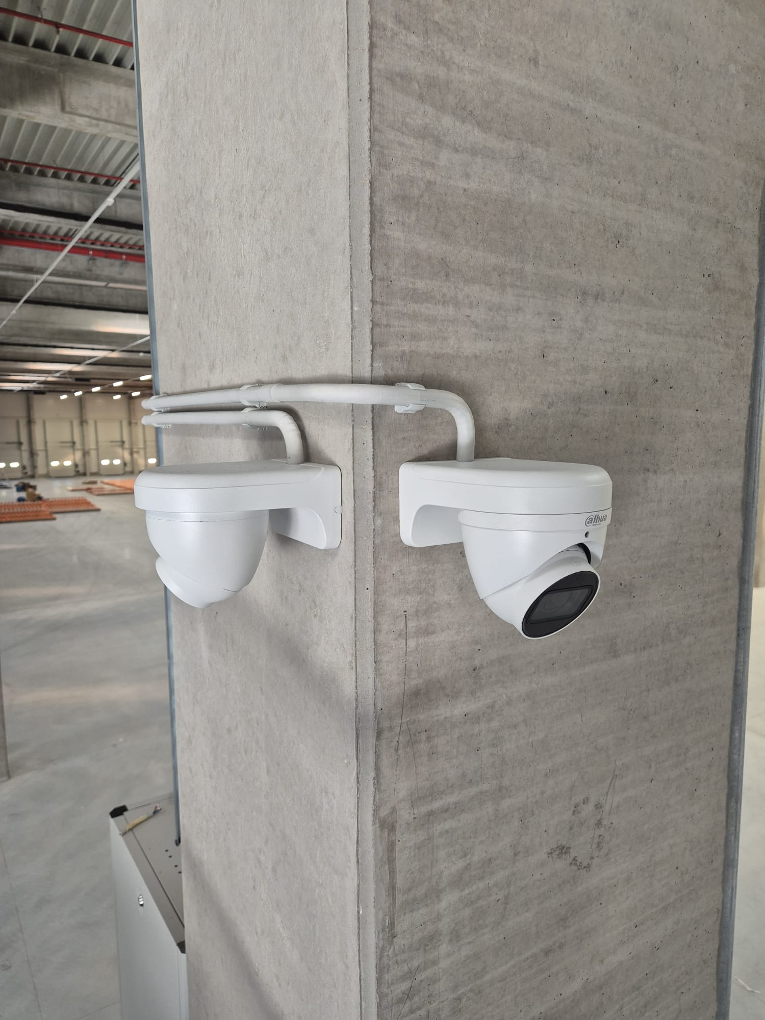 Twee beveiligingscamera&rsquo;s met opbouwleidingwerk aan een betonnen kolom in een nog lege bedrijfsloods
