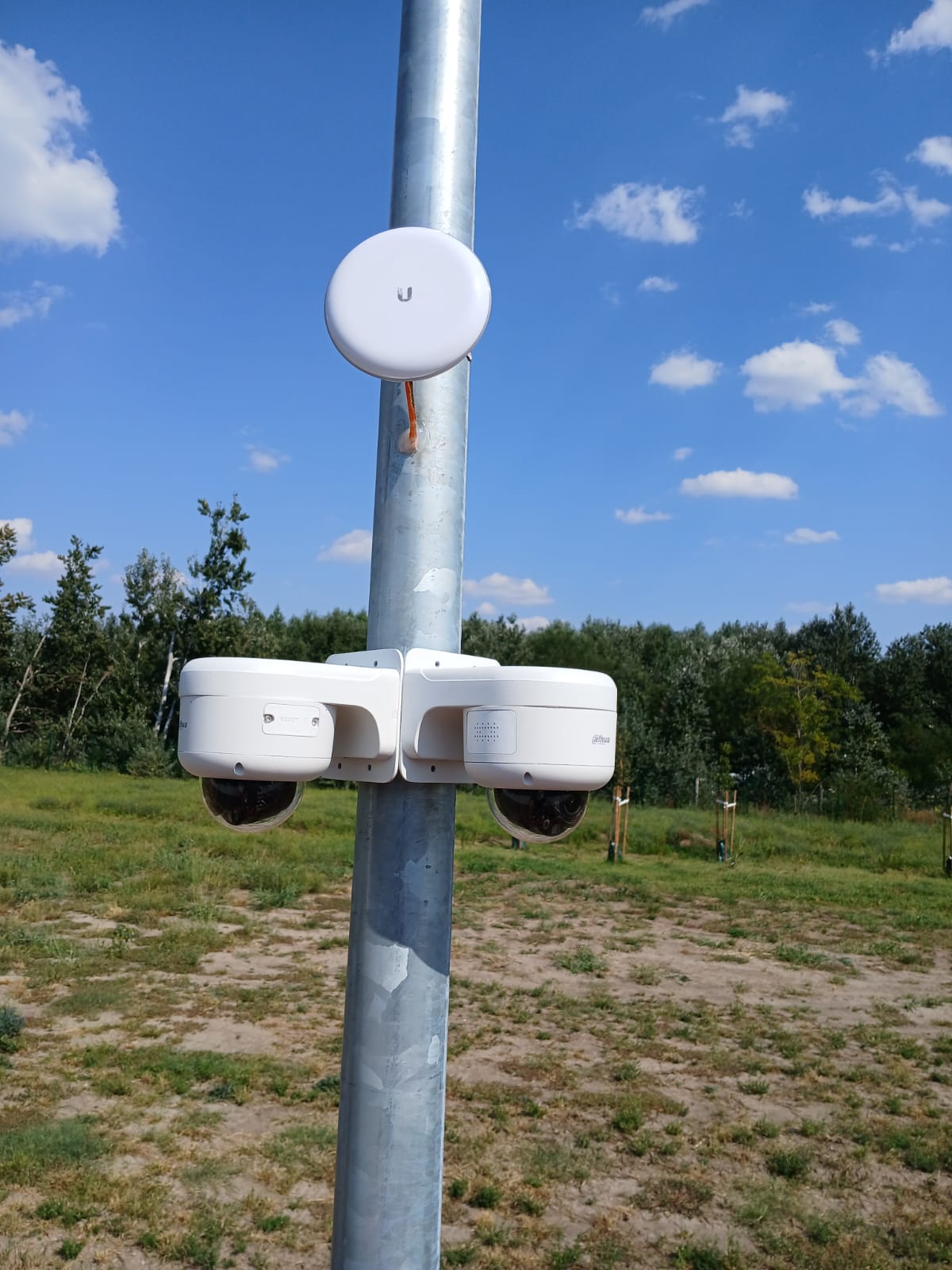 Twee witte Dahua domecamera's en een draadloze verbinding aan een stalen mast op een open terrein